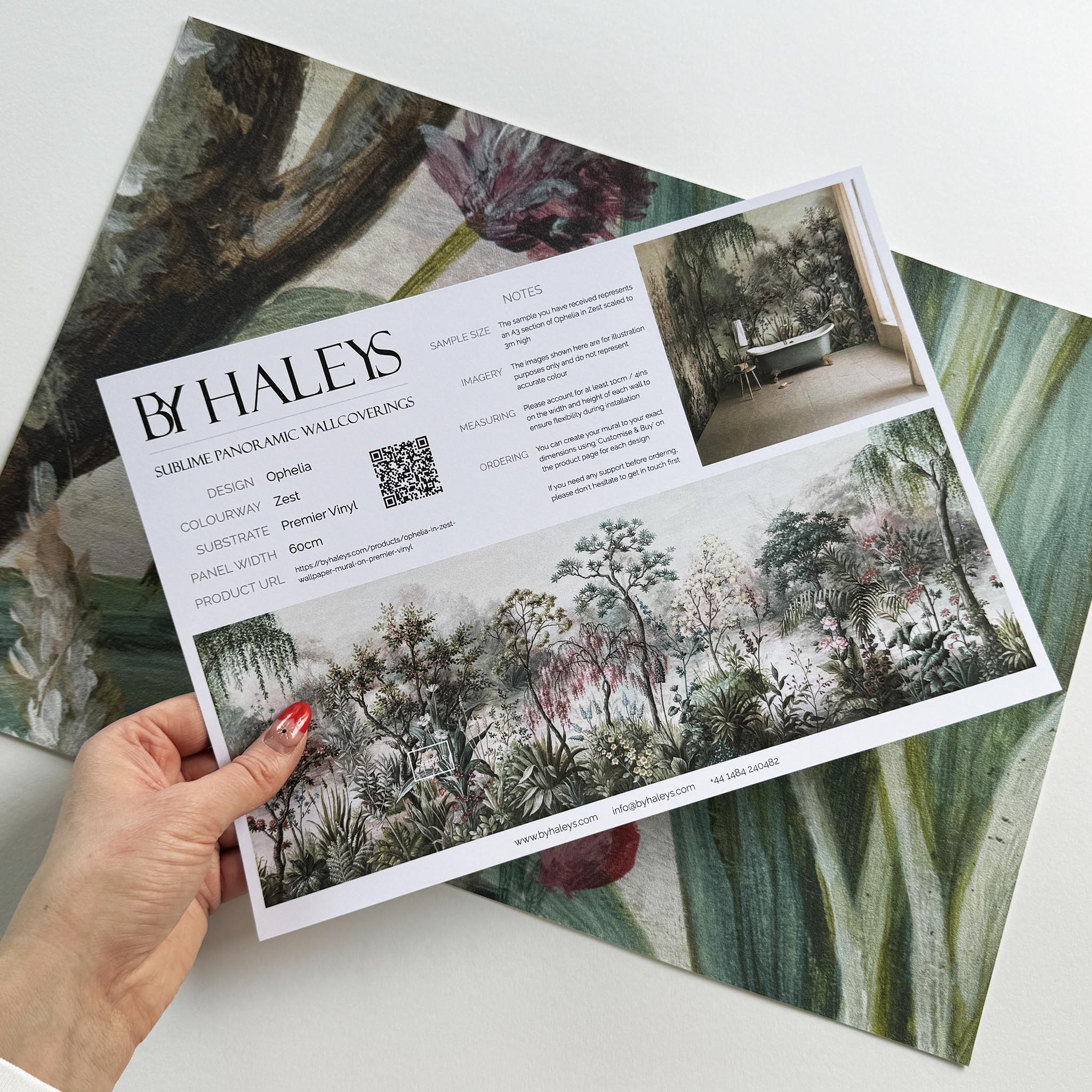 A hand showing information for a vinyl wallpaper mural sample which features a lakeside garden scene in mint and pink.