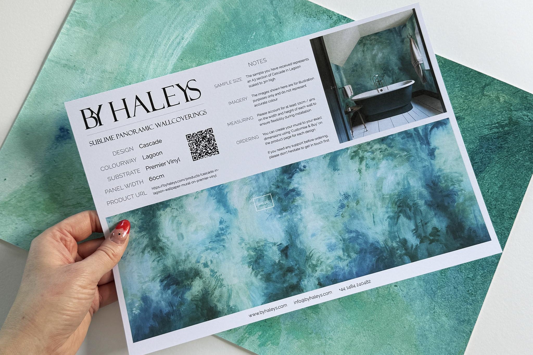 A hand showing information for a vinyl wallpaper mural sample which features an abstract wash in aqua and jade.