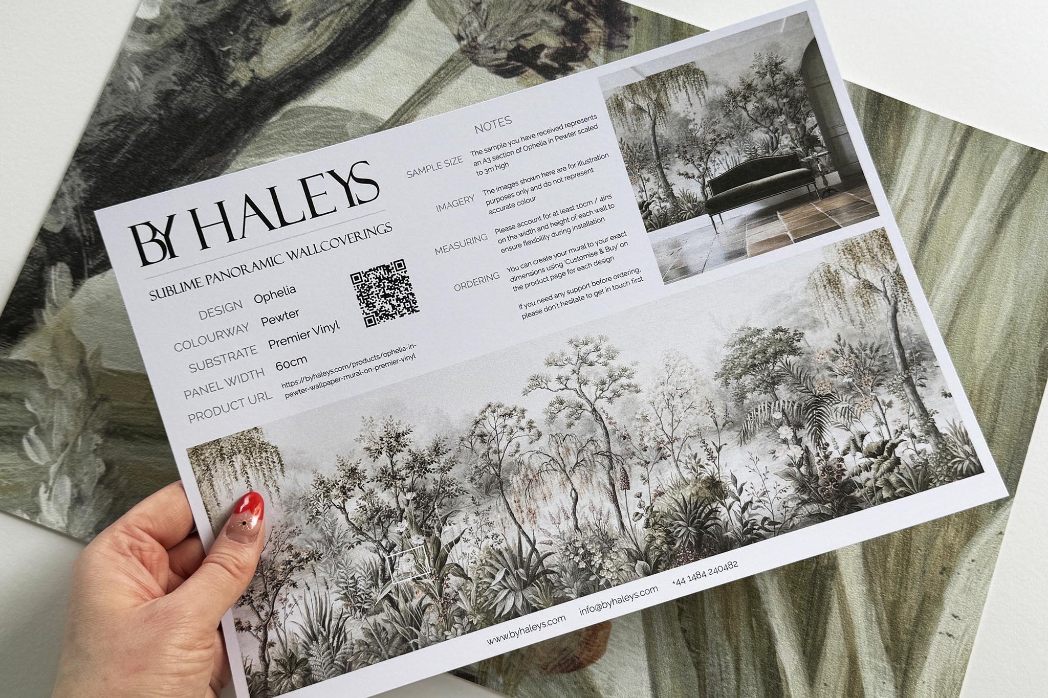 A hand showing information for a vinyl wallpaper mural sample which features a lakeside scene in grey and peach.