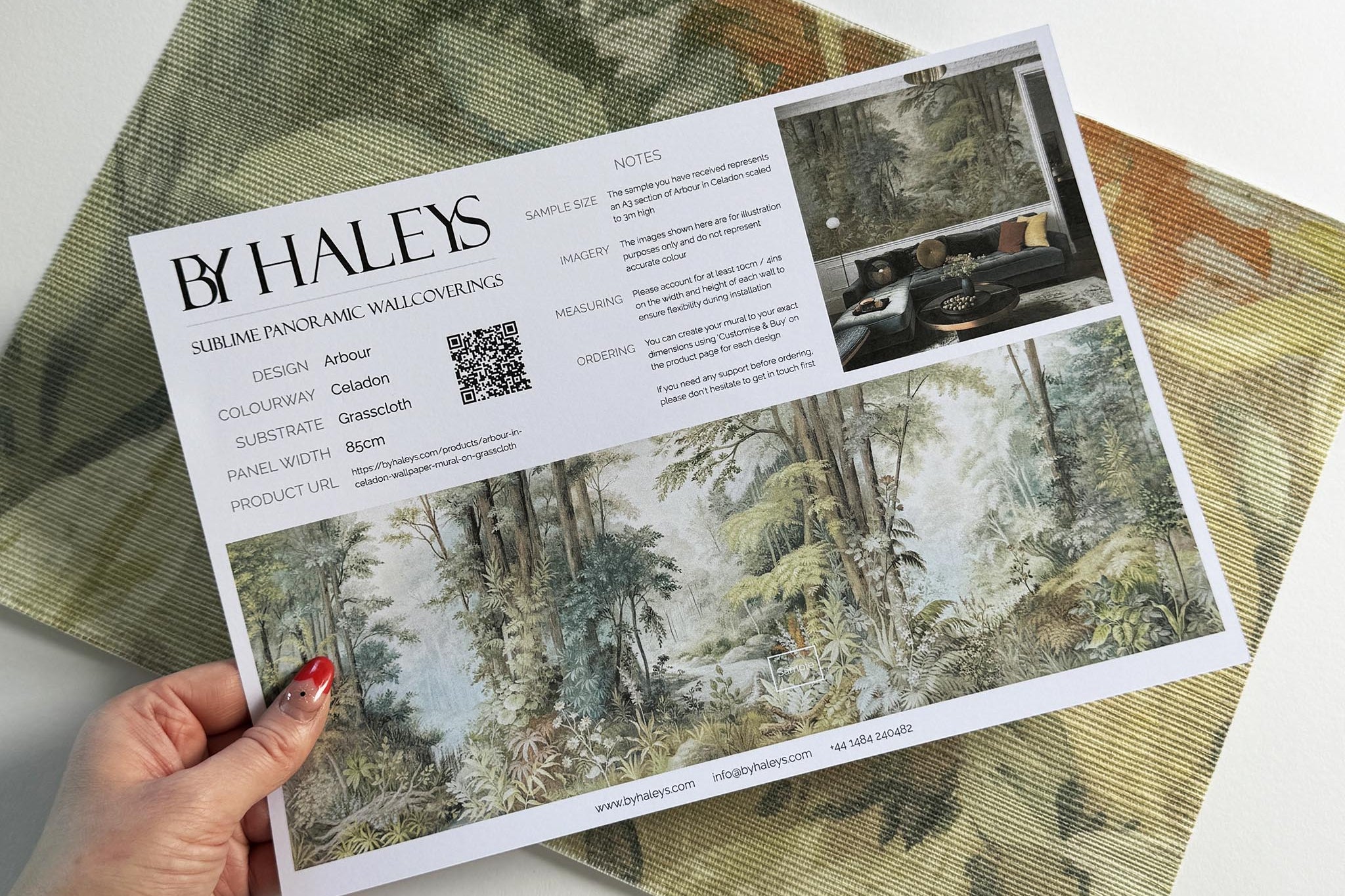 A hand showing information for a grasscloth wallpaper mural sample which features an airy woodland in sage, yellow, and mist.