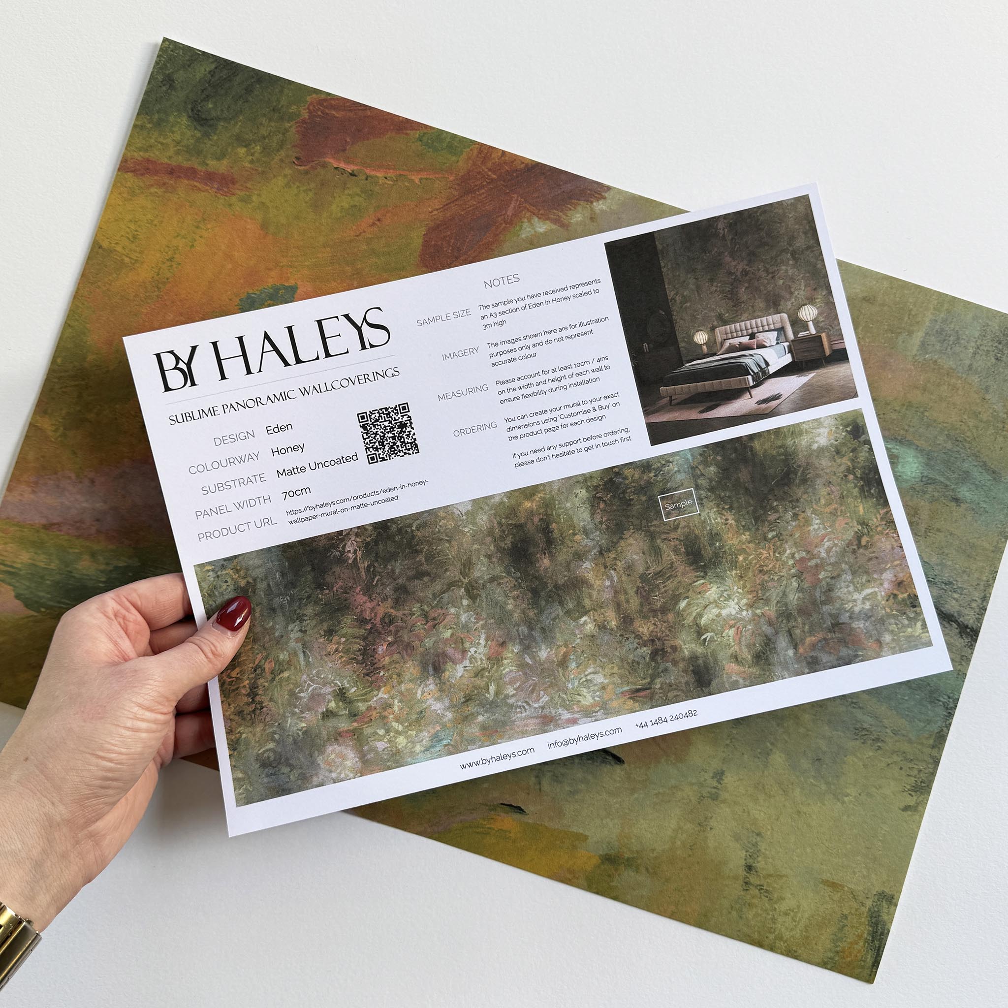 A hand showing information for a matte wallpaper mural sample which features a abstract layering of ochre and teal.