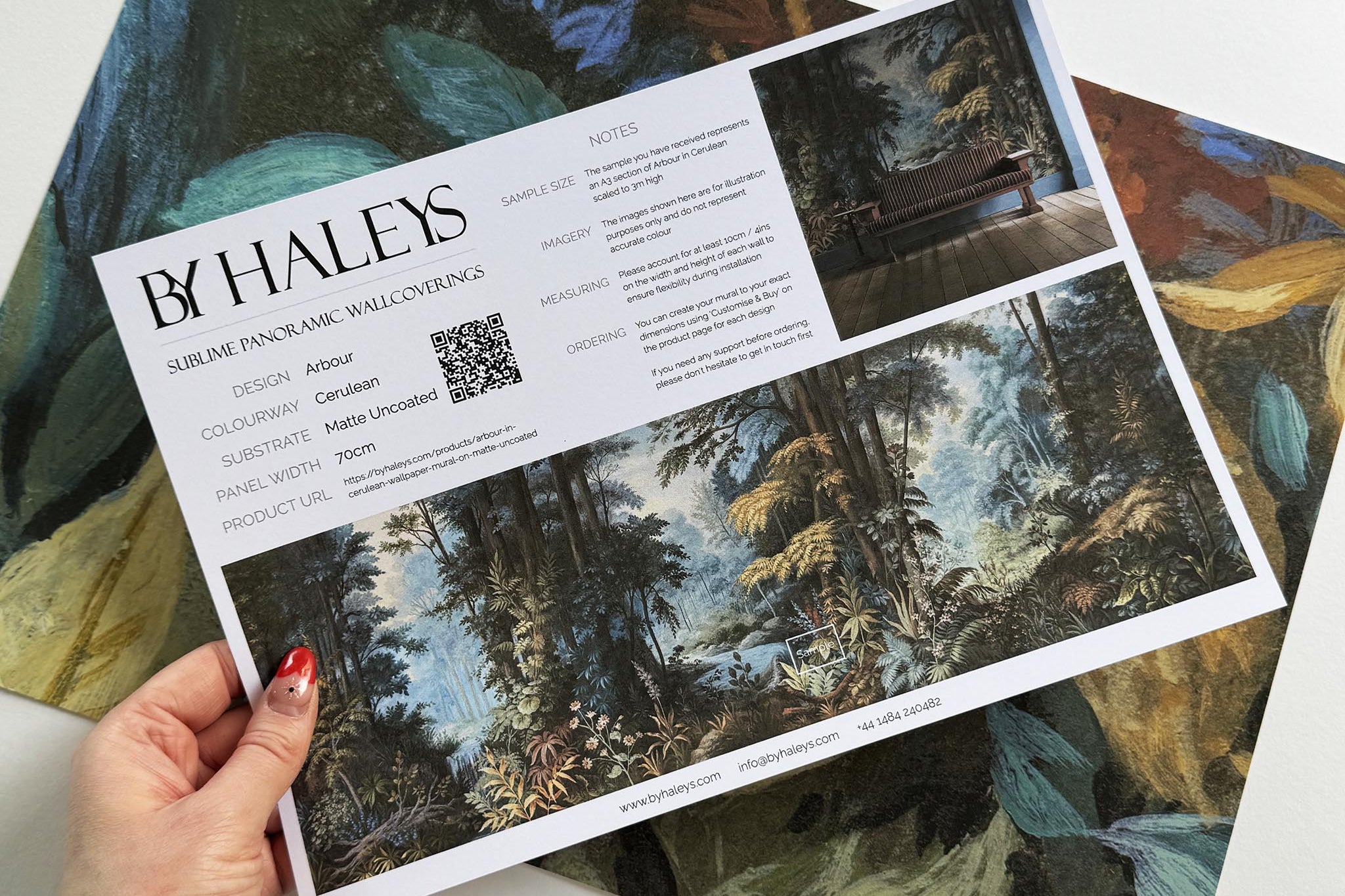 A hand showing information for a matte wallpaper mural sample which features an enchanted forest in blue and rust.