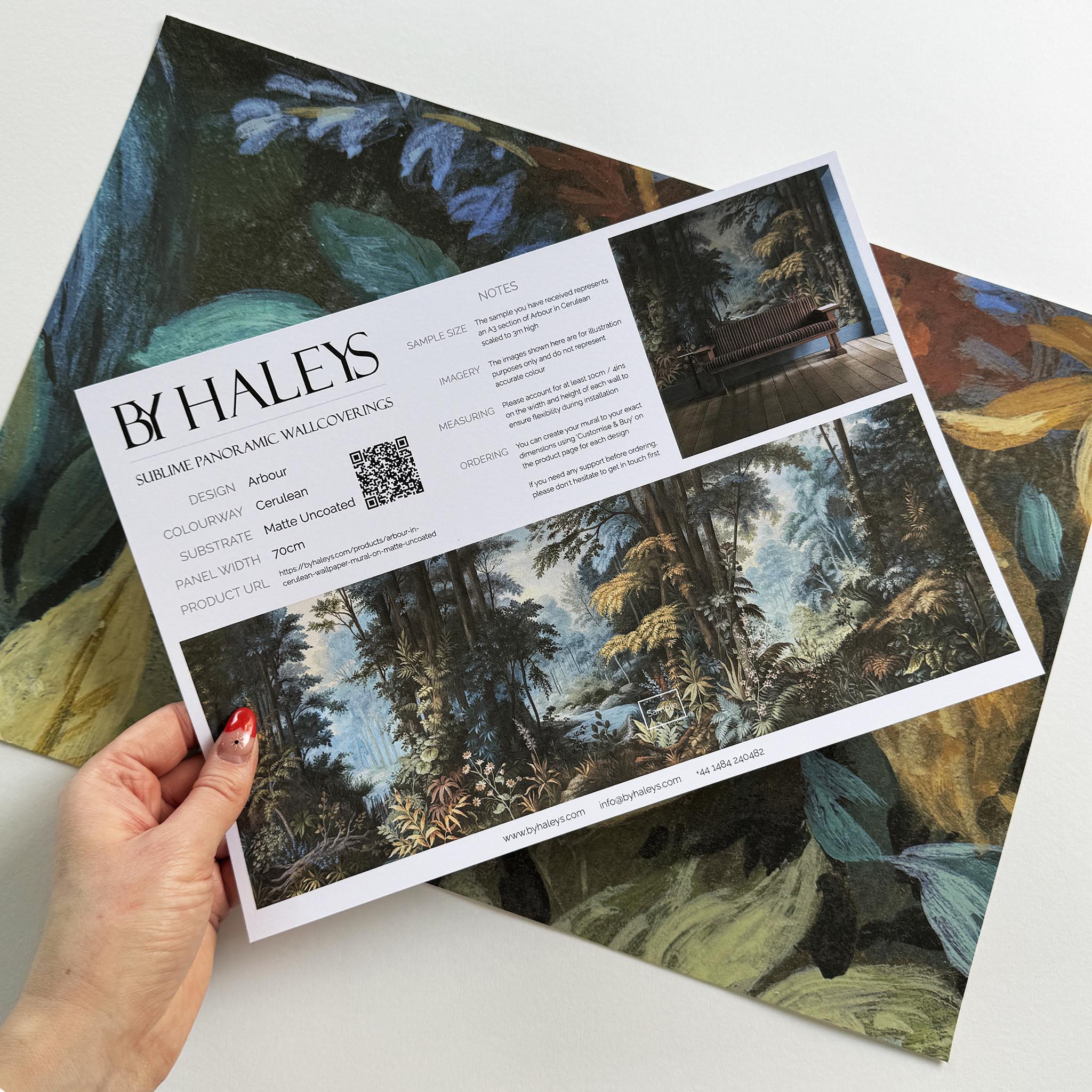 A hand showing information for a matte wallpaper mural sample which features an enchanted forest in blue and rust.