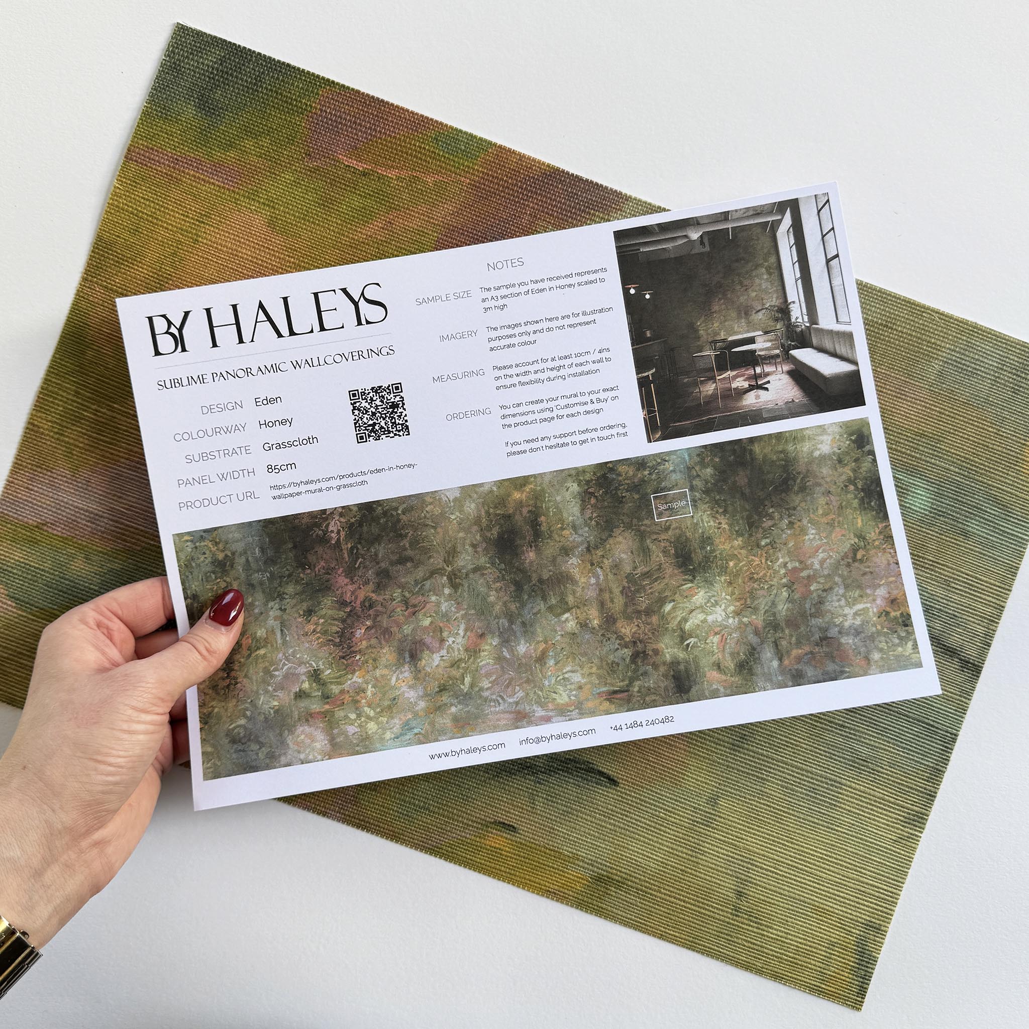 A hand showing information for a grasscloth wallpaper mural sample which features a abstract layering of ochre and teal.