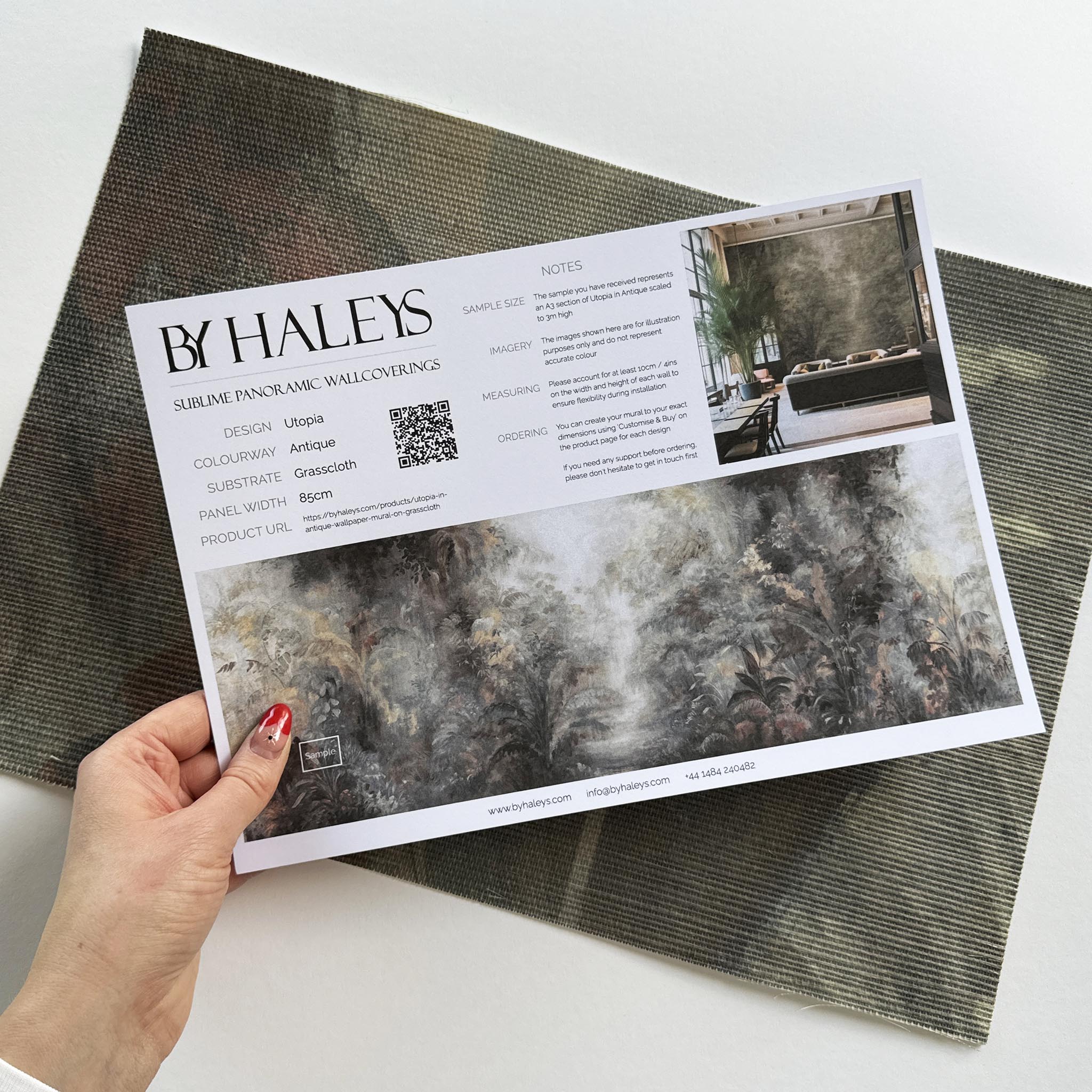 A hand showing information for a grasscloth wallpaper mural sample which features a rainforest in lavender and rust.