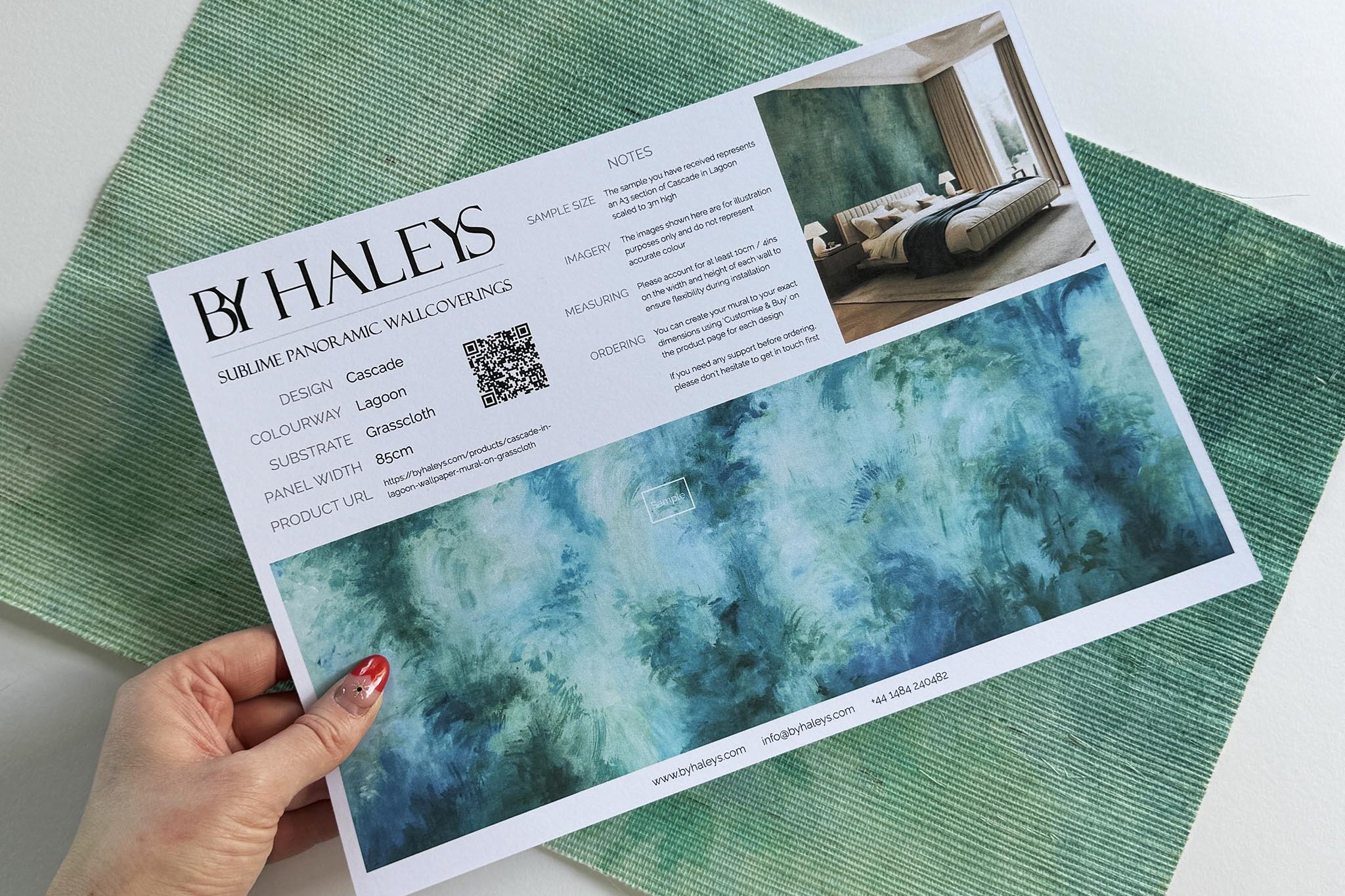 A hand showing information for a grasscloth wallpaper mural sample which features an abstract wash in aqua and jade.