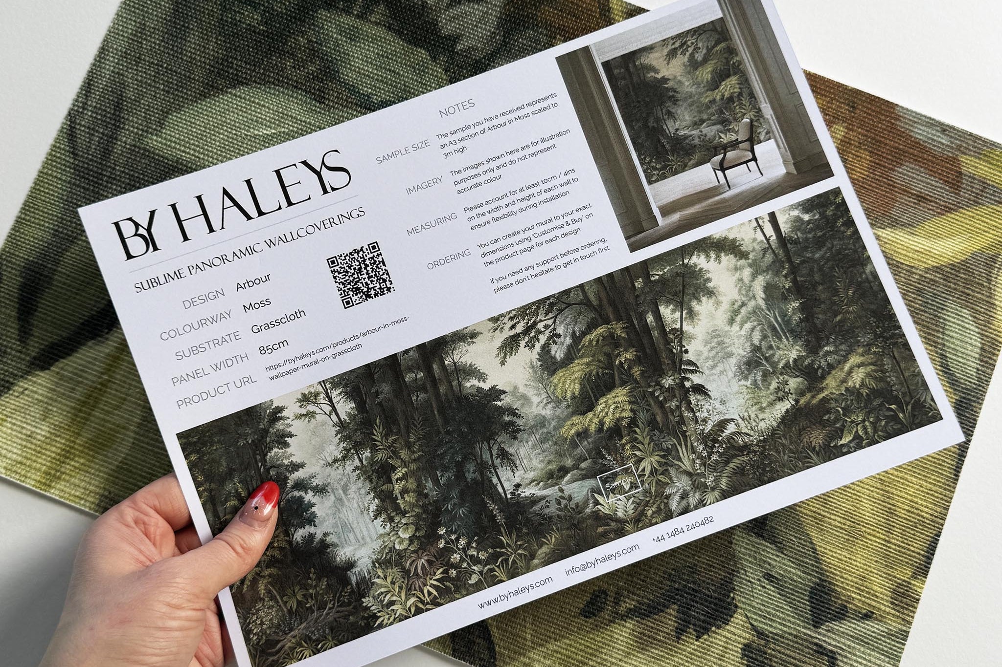A hand showing information for a grasscloth wallpaper mural sample which features a misty woodland in sage and ochre.