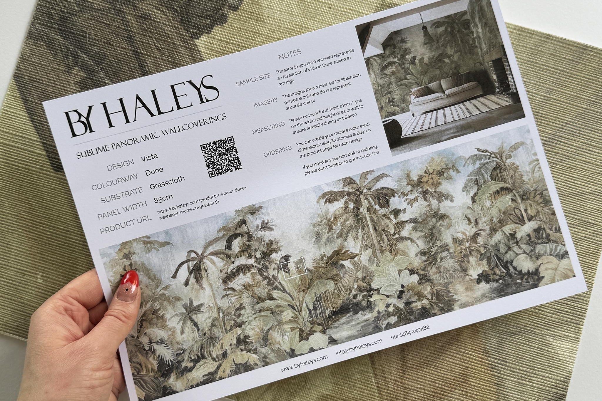 A hand showing information for a grasscloth wallpaper mural sample which features a jungle scene in sepia and blue.