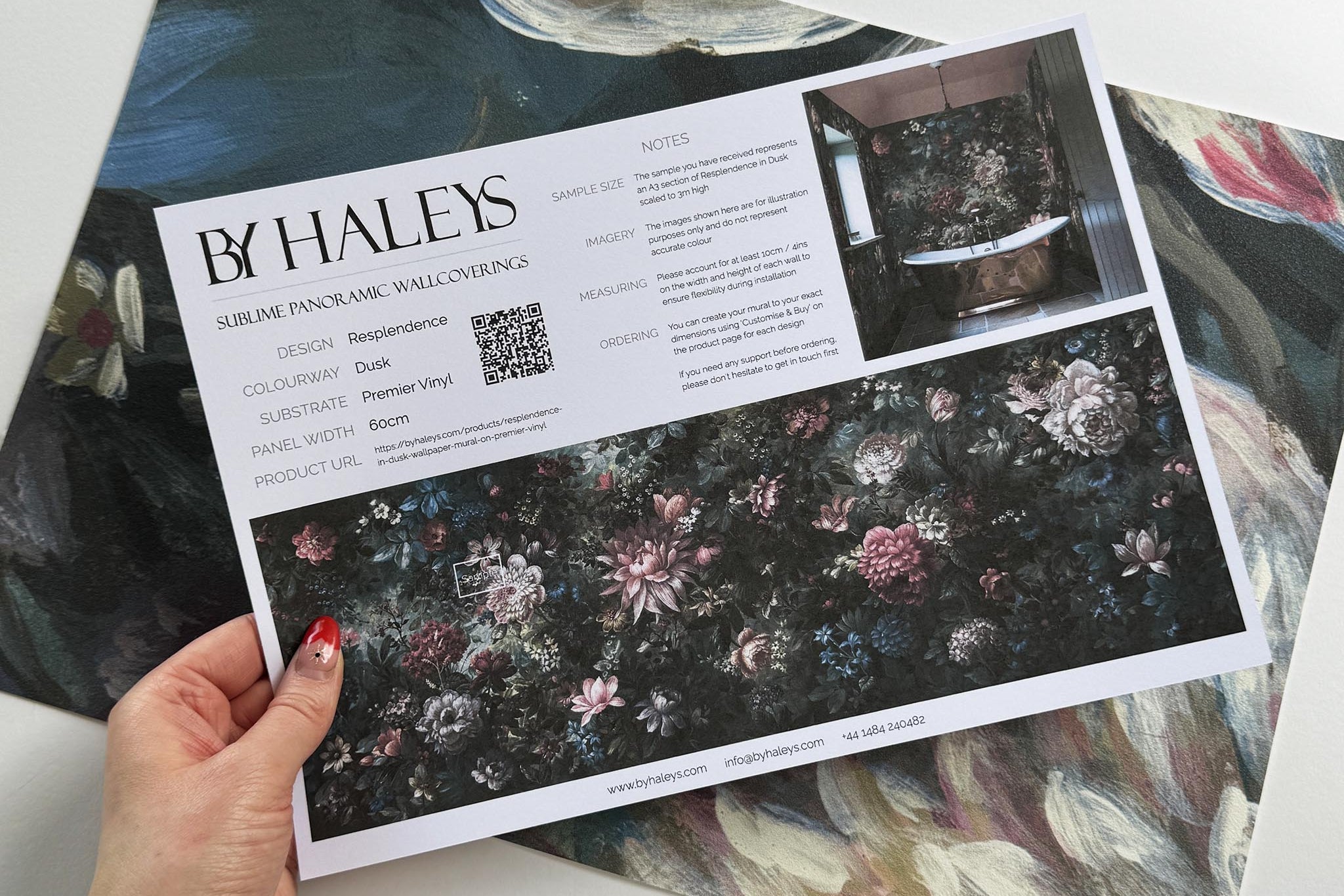 A hand showing information for a vinyl wallpaper mural sample which features a floral bloom in crimson and blue.