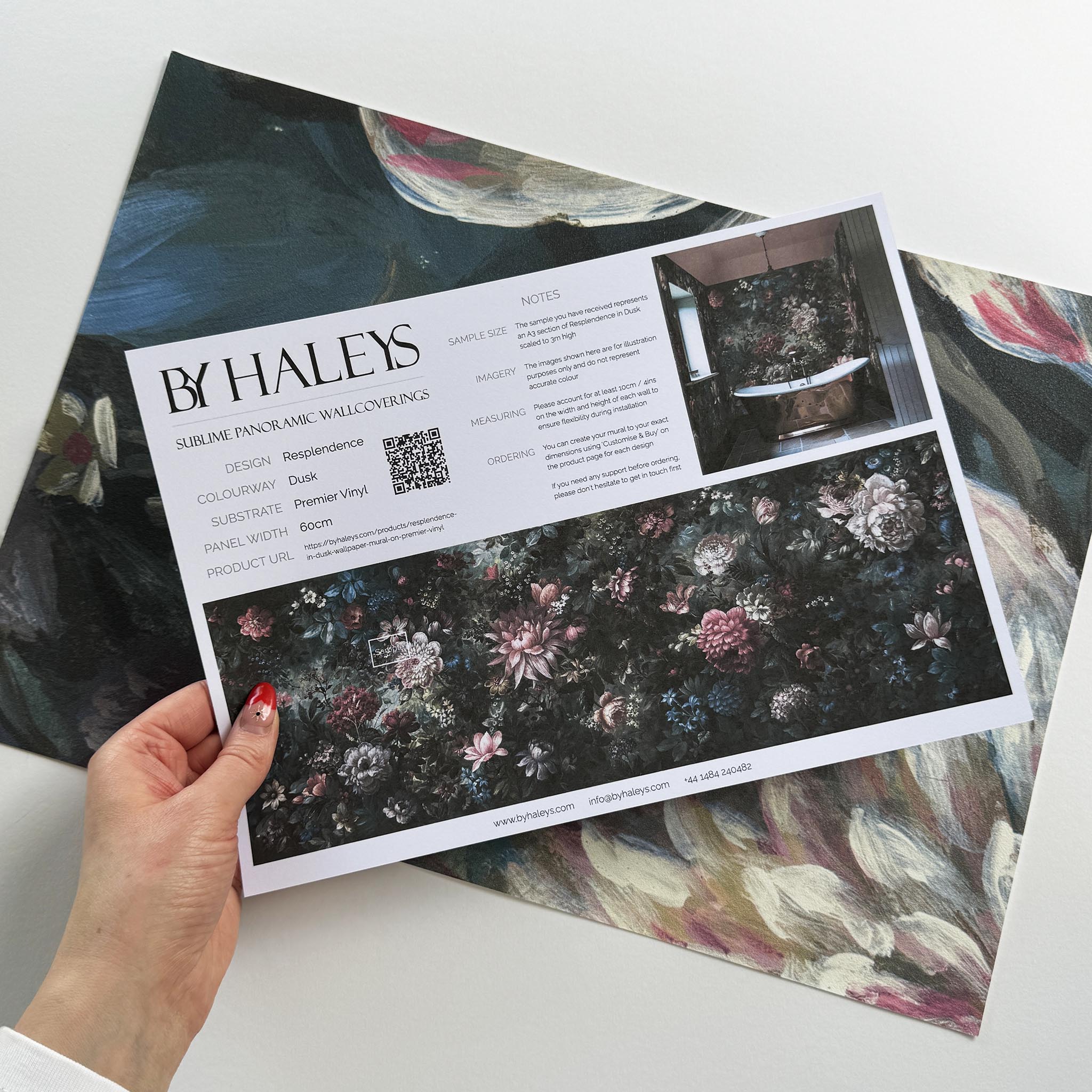 A hand showing information for a vinyl wallpaper mural sample which features a floral bloom in crimson and blue.