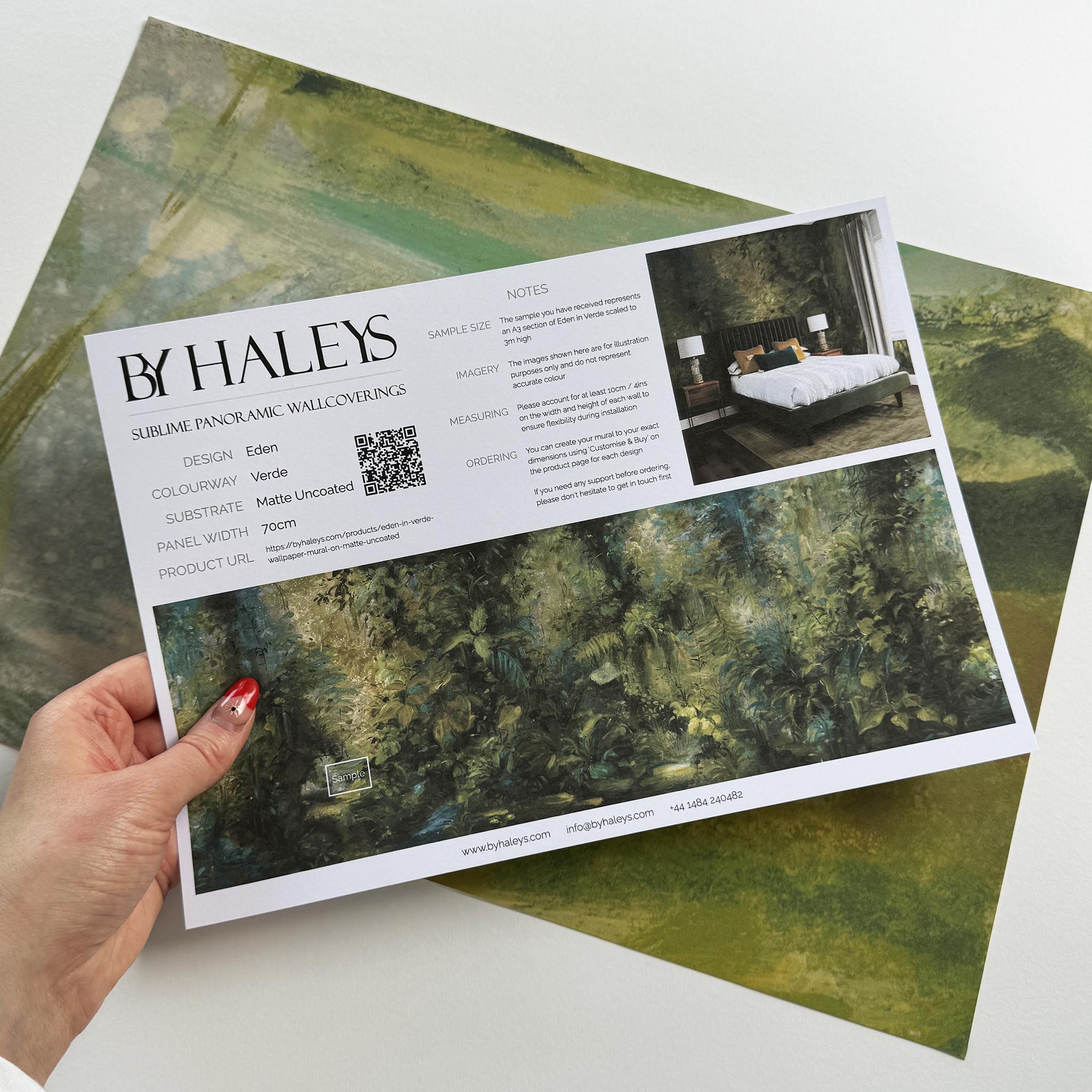 A hand showing information for a matte wallpaper mural sample which features a jungle abstraction in emerald and ochre.
