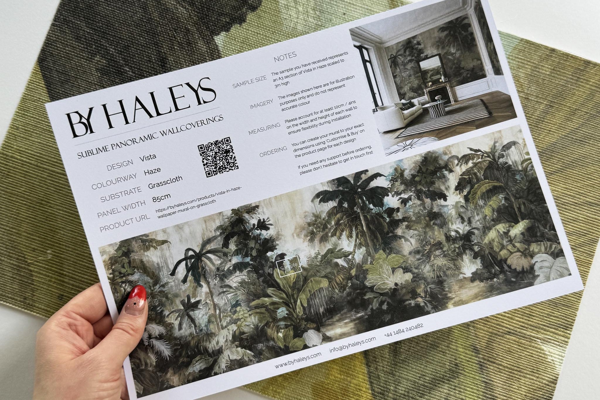 A hand showing information for a grasscloth wallpaper mural sample which features a tropical scene in sage and parchment.
