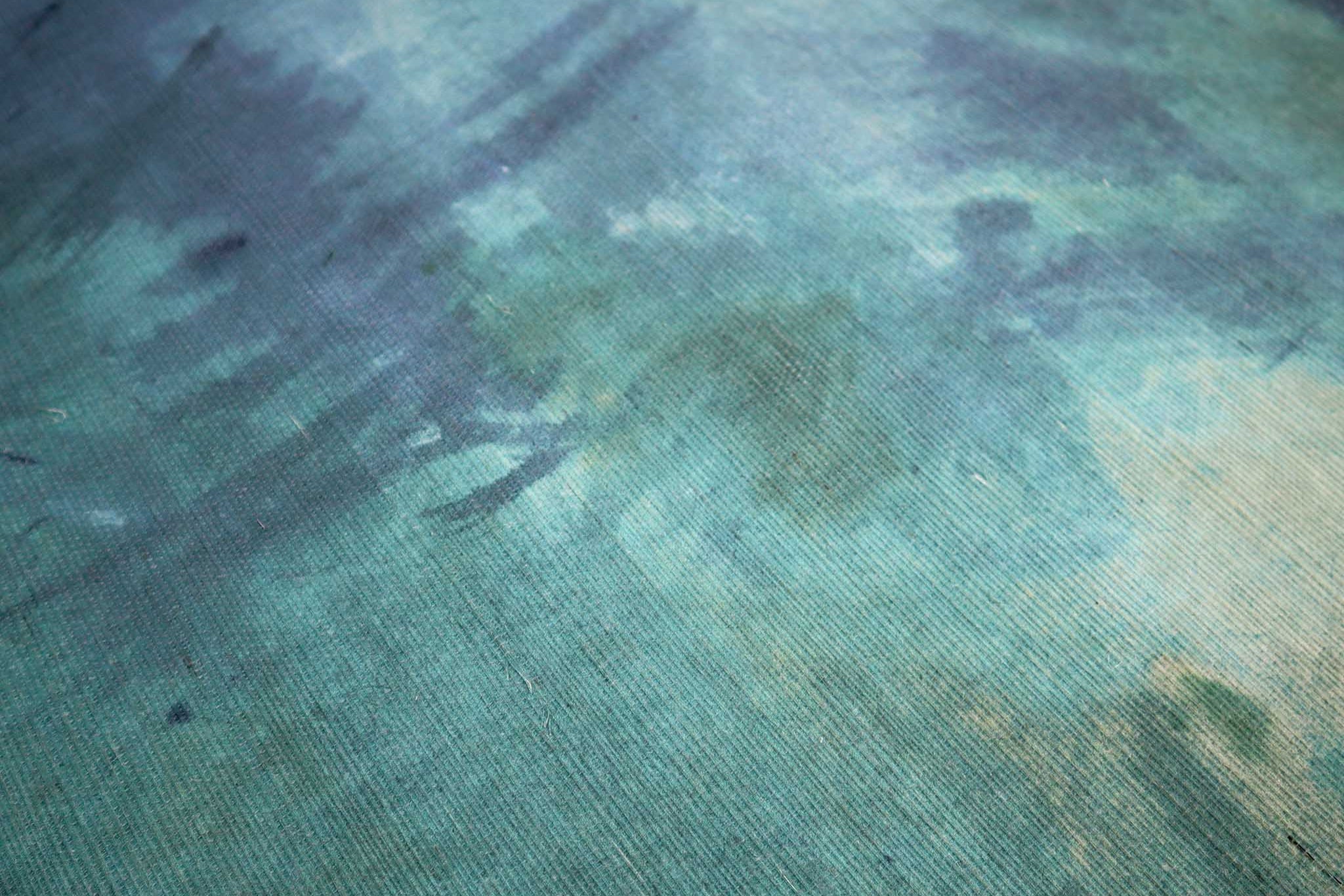 Close-up of a textured grasscloth wallpaper mural featuring fluid aqua and teal tones and painterly brush strokes.