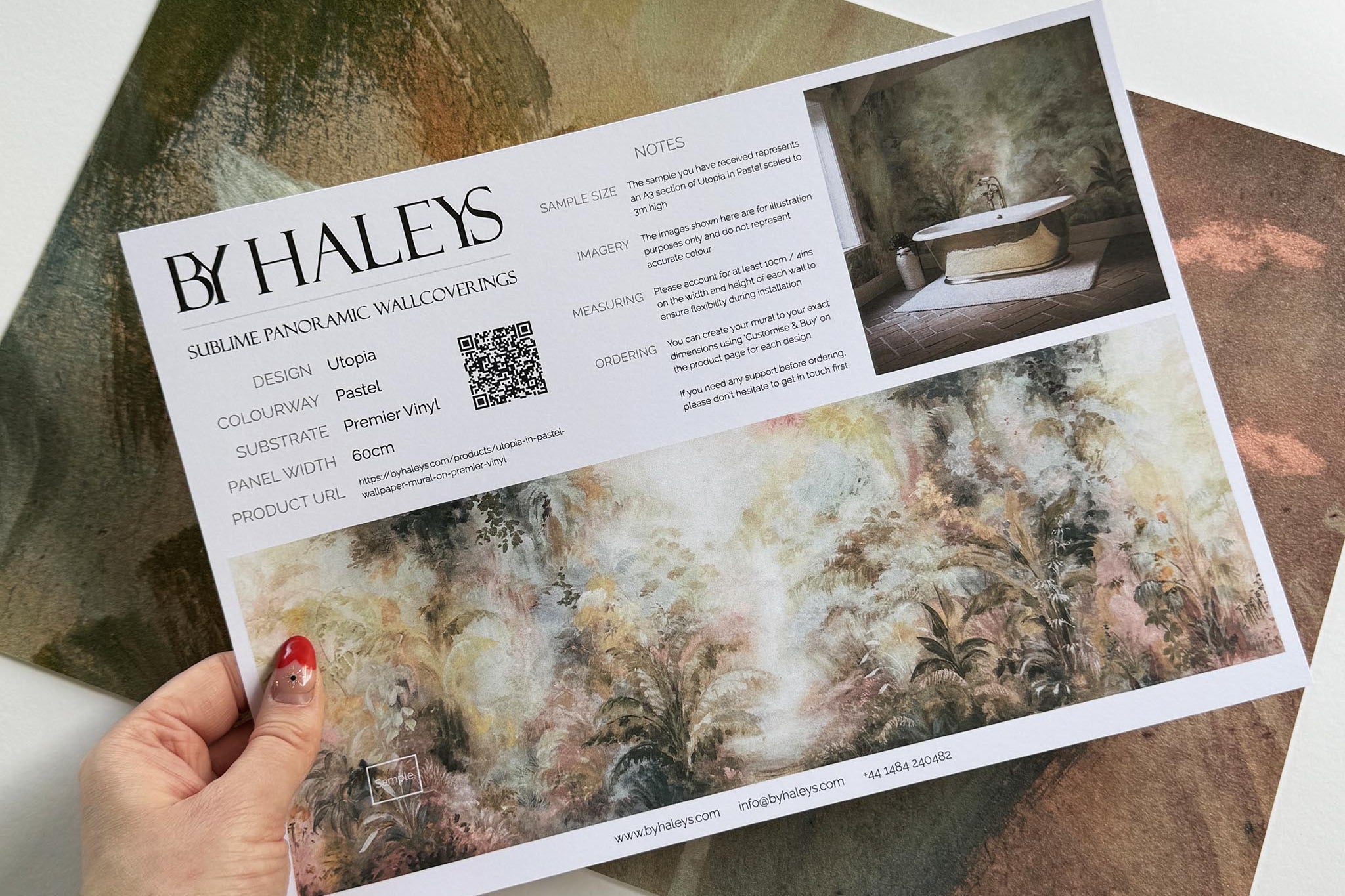 A hand showing information for a vinyl wallpaper mural sample which features a rainforest in blush and sky blue.