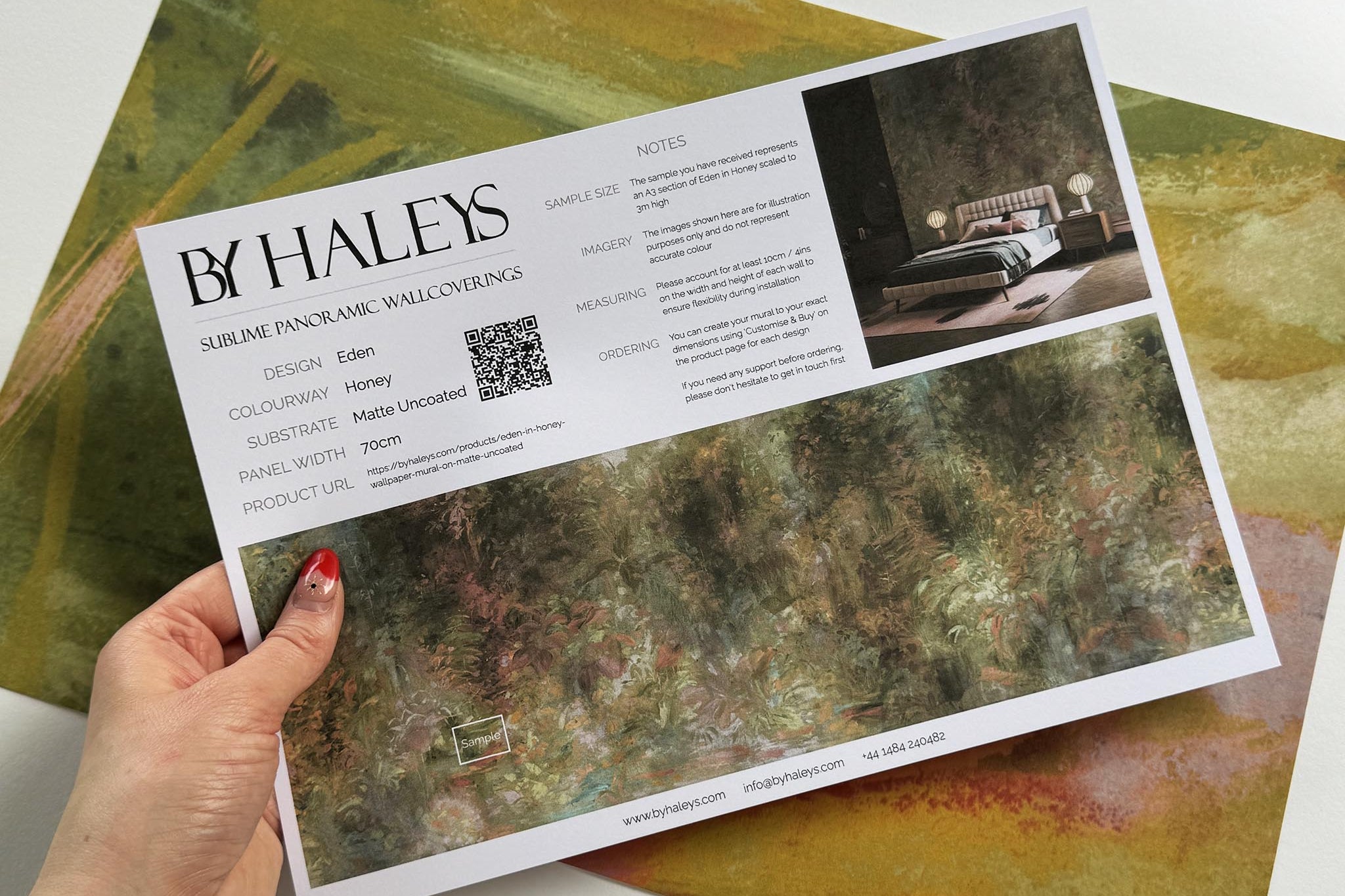 A hand showing information for a matte wallpaper mural sample which features a abstract layering of ochre and teal.