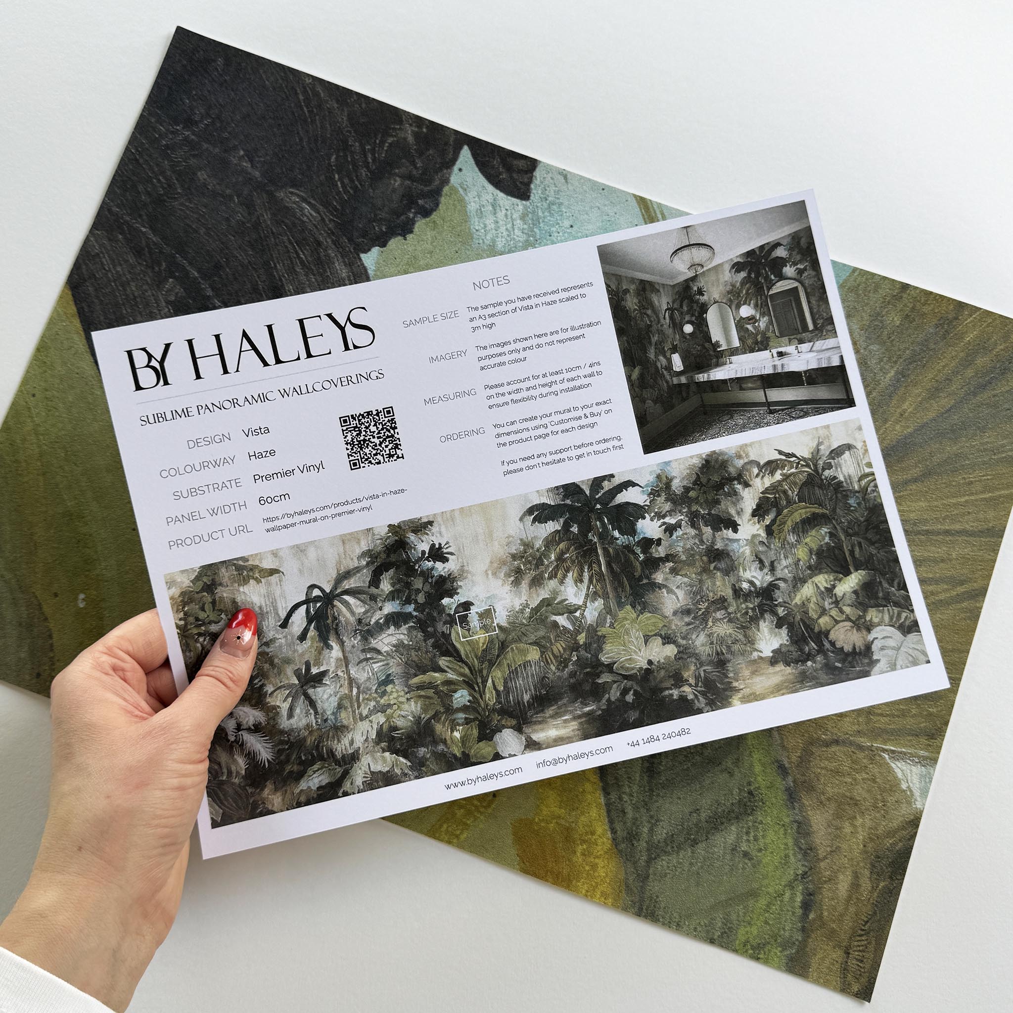 A hand showing information for a vinyl wallpaper mural sample which features a tropical scene in sage and parchment.