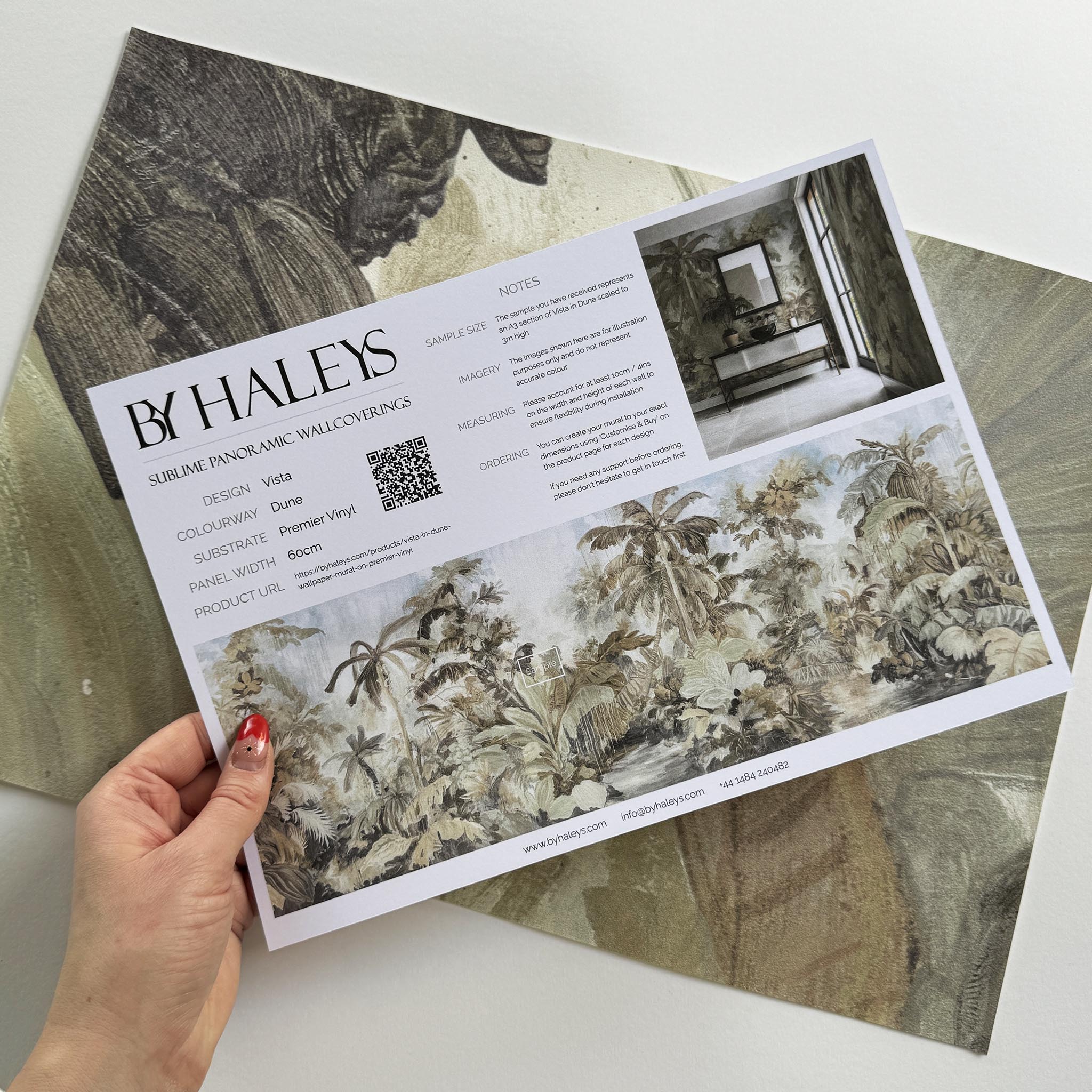 A hand showing information for a vinyl wallpaper mural sample which features a jungle scene in sepia and blue.