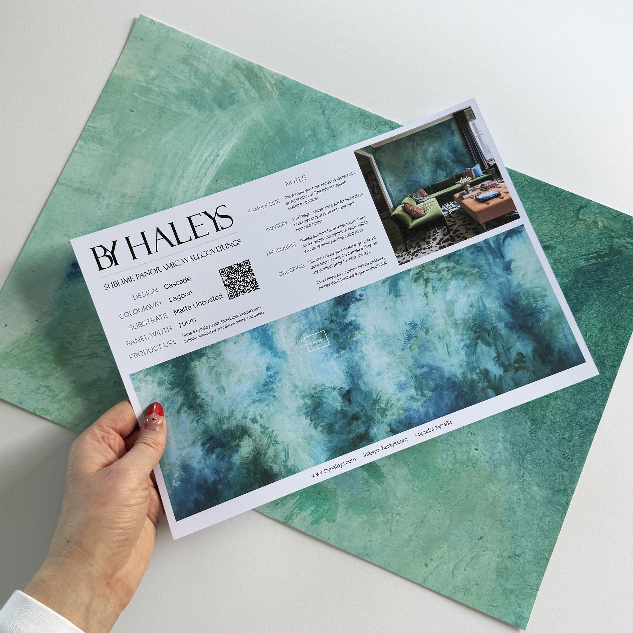 A hand showing information for a matte wallpaper mural sample which features an abstract wash in aqua and jade.