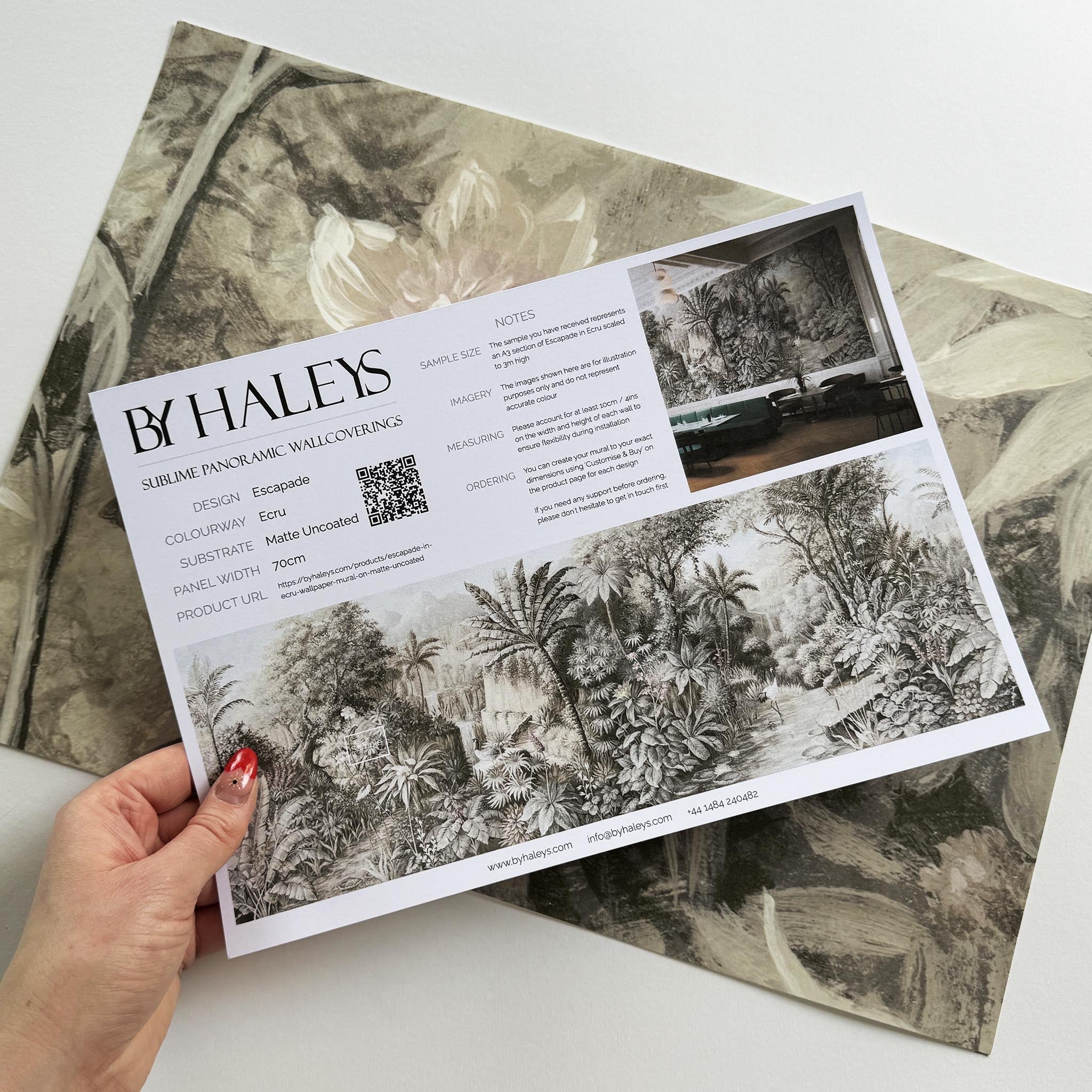 A hand showing information for a matte wallpaper mural sample which features a jungle vista in sepia and blush.