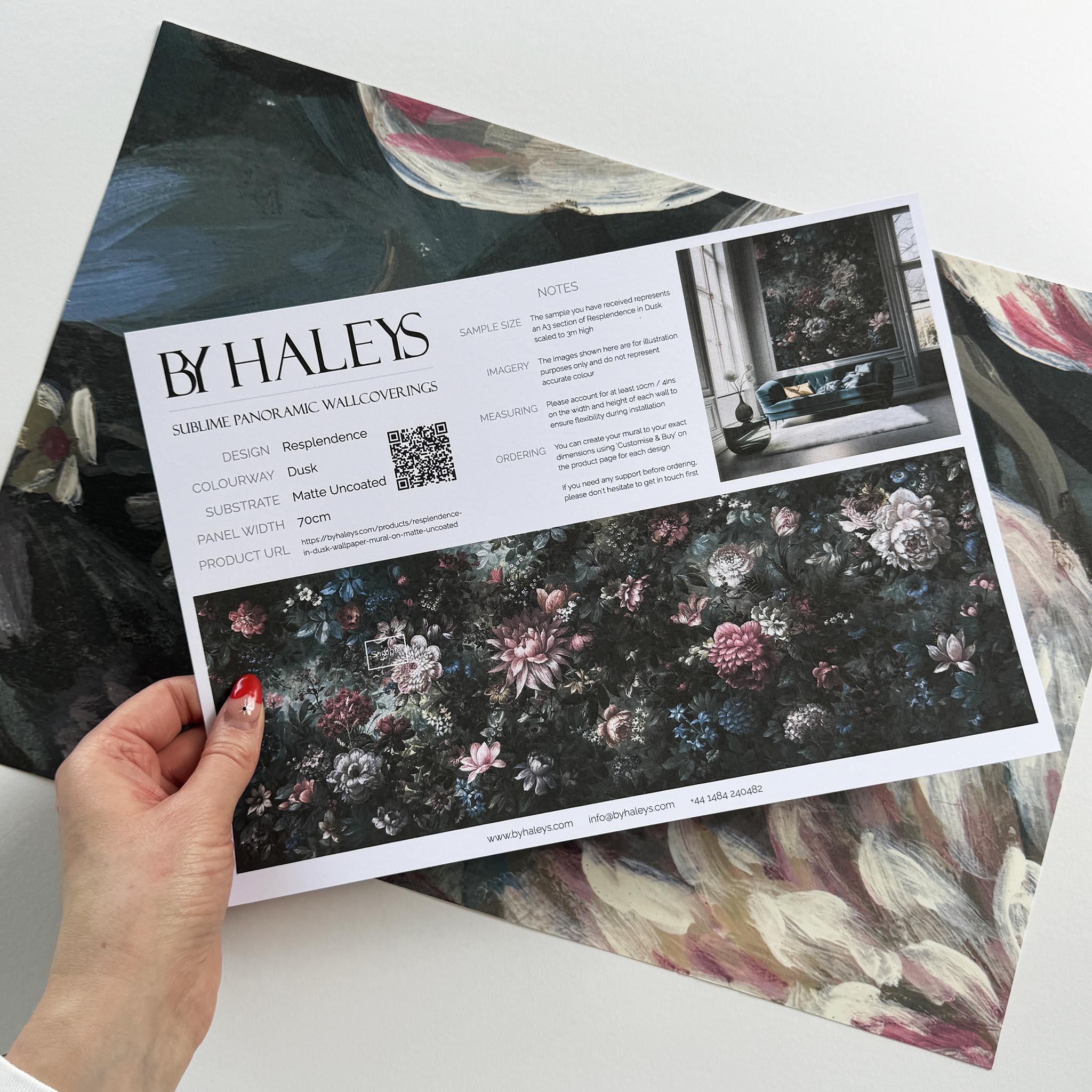 A hand showing information for a matte wallpaper mural sample which features a floral bloom in crimson and blue.