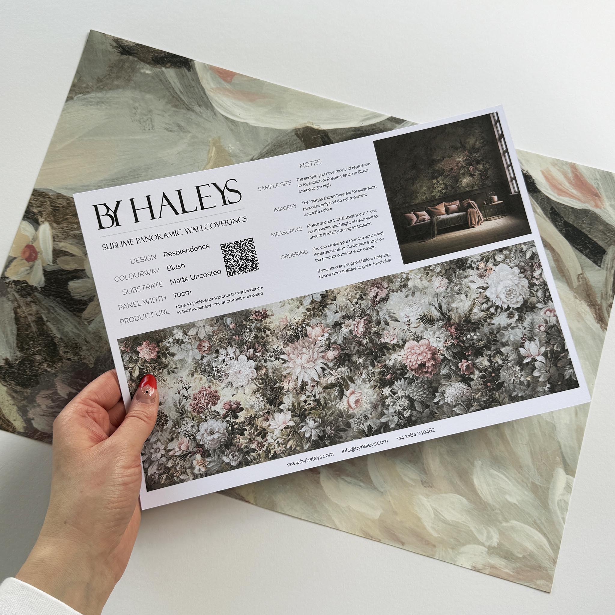 A hand showing information for a matte wallpaper mural sample which features a floral composition in soft neutrals.