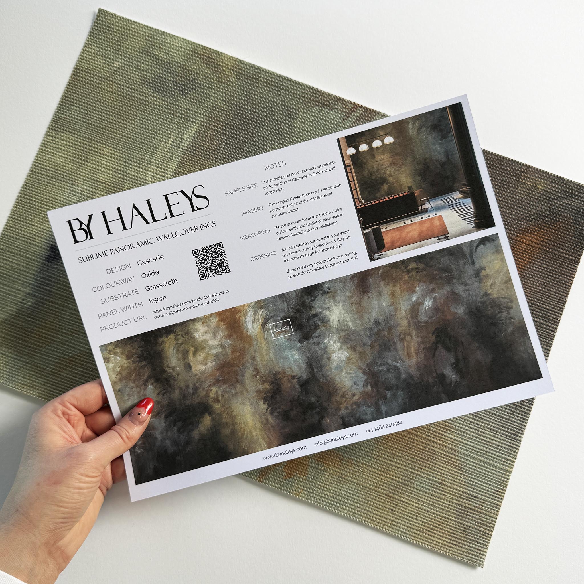 A hand showing information for a grasscloth wallpaper mural sample which features an abstract haze in charcoal and ash.