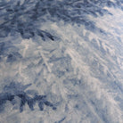 A close up view showing the detail of a grasscloth wallpaper mural which features soft blue woodland