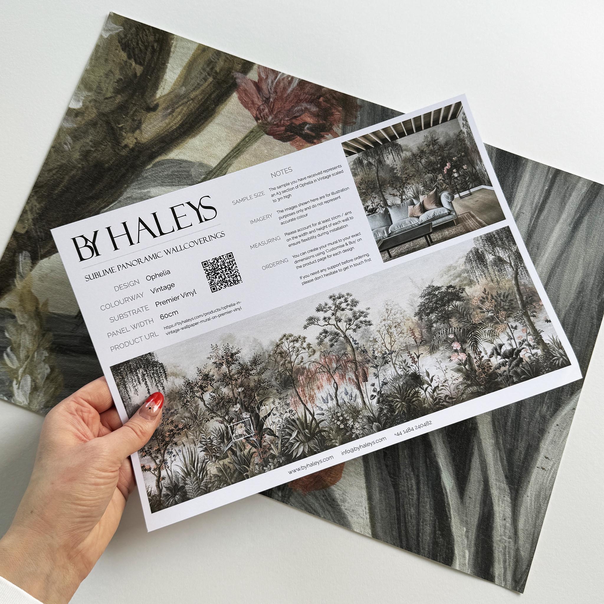 A hand showing information for a vinyl wallpaper mural sample which features a lakeside scene in vintage tones.