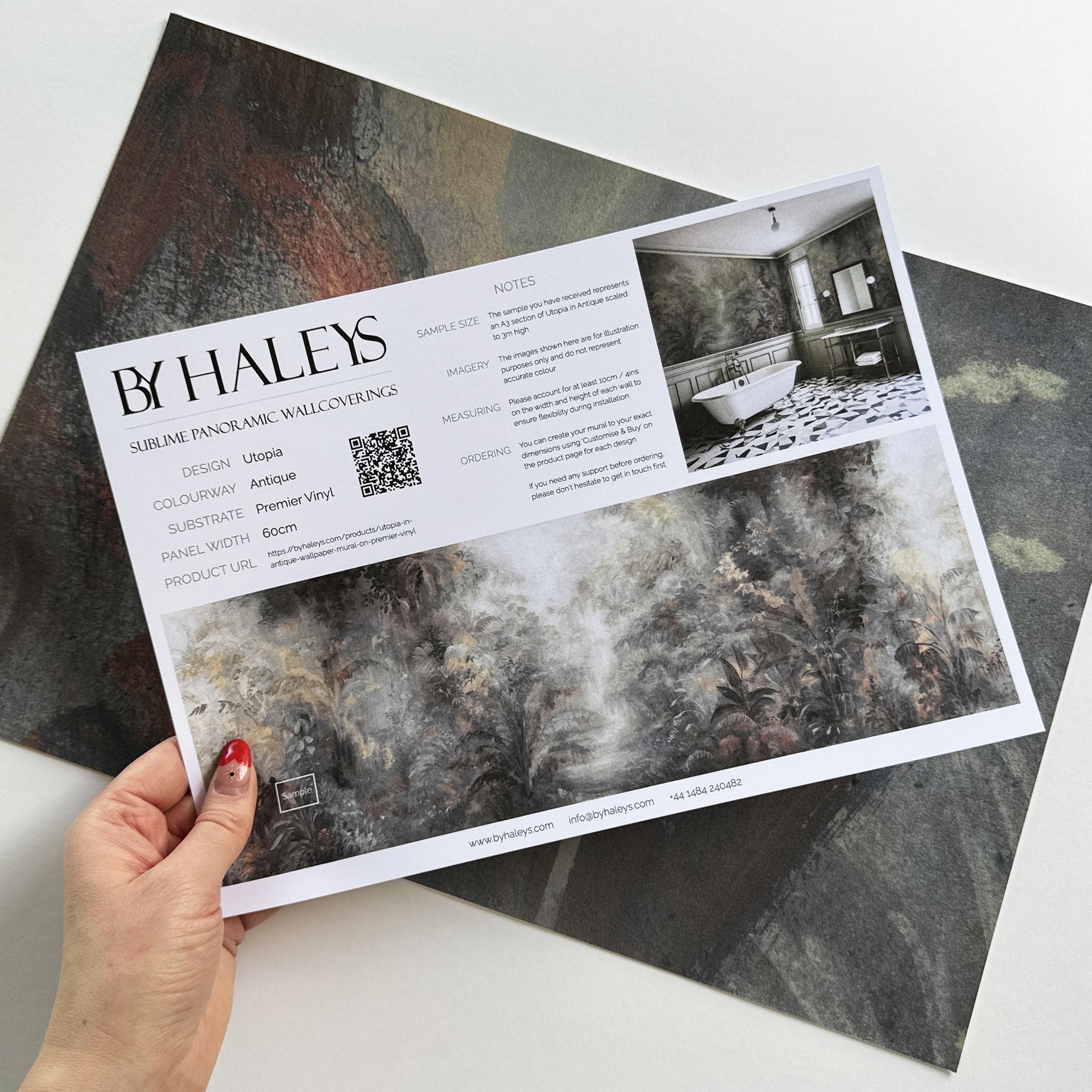 A hand showing information for a vinyl wallpaper mural sample which features a rainforest in lavender and rust.