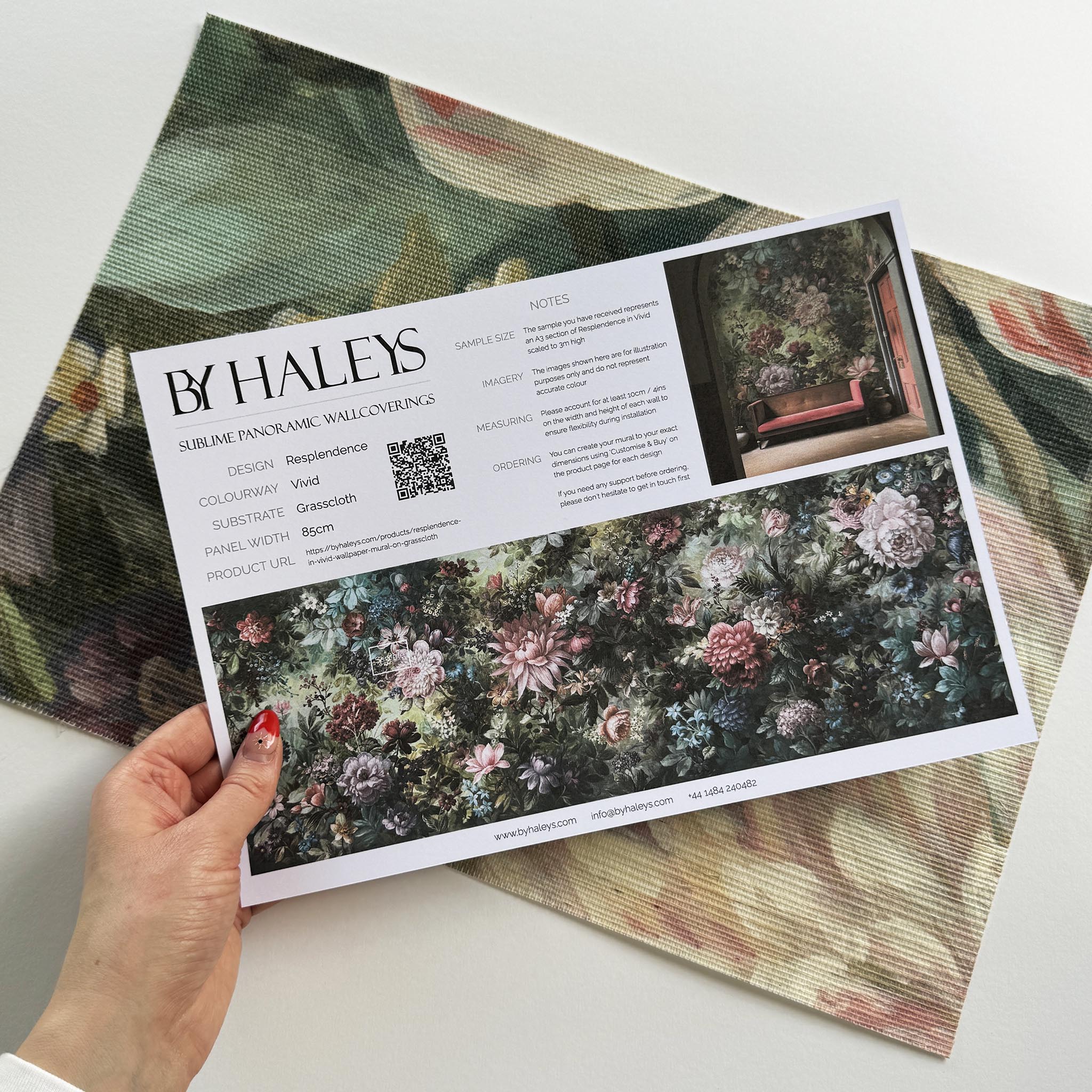 A hand showing information for a grasscloth wallpaper mural sample which features a floral tapestry in rich jewel tones.