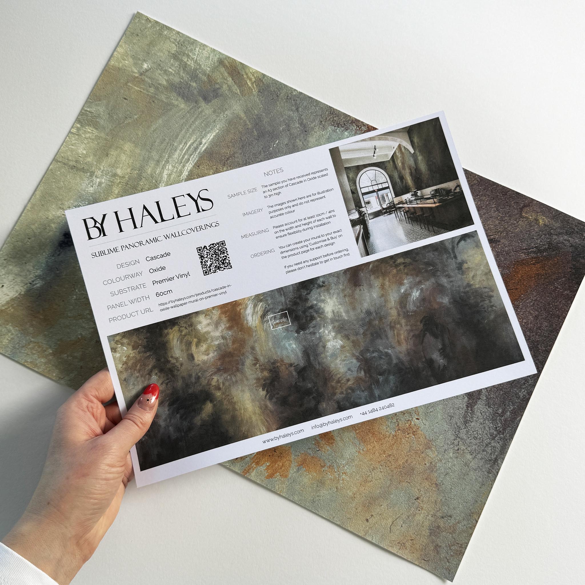 A hand showing information for a vinyl wallpaper mural sample which features an abstract haze in charcoal and ash.