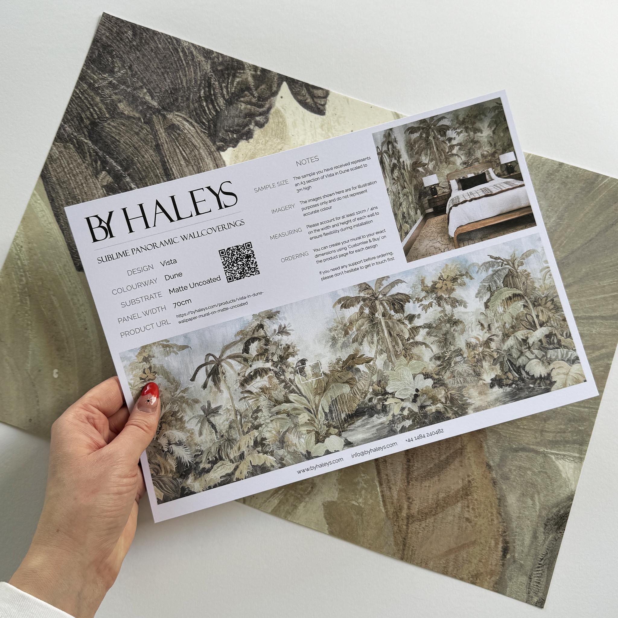A hand showing information for a matte wallpaper mural sample which features a jungle scene in sepia and blue.