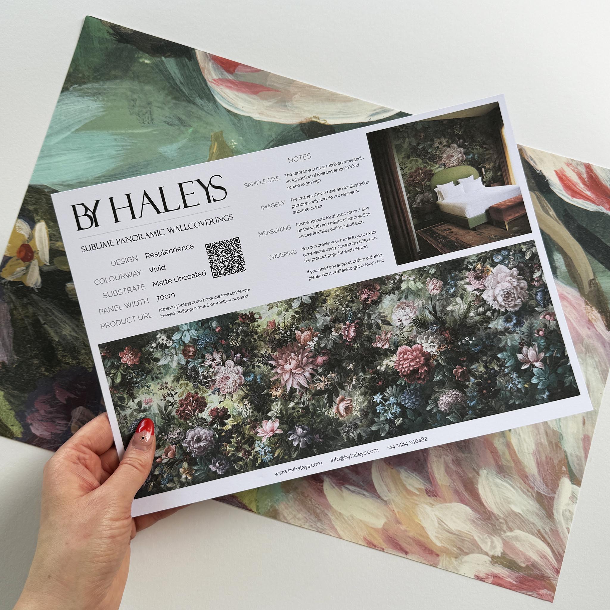 A hand showing information for a matte wallpaper mural sample which features a floral tapestry in rich jewel tones.