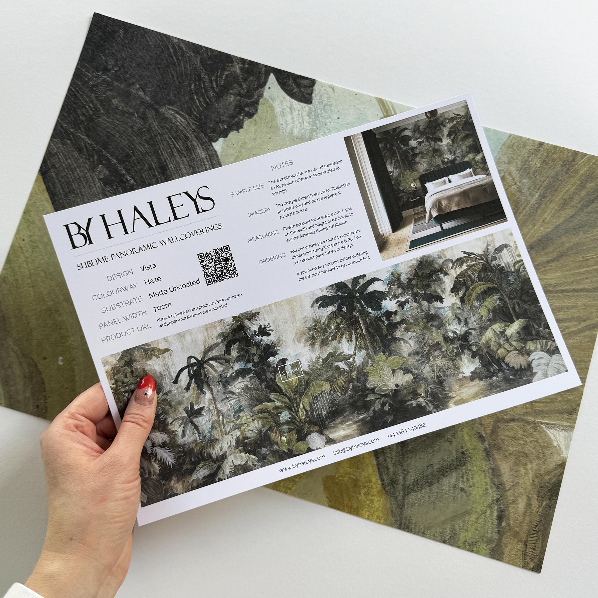 A hand showing information for a matte wallpaper mural sample which features a tropical scene in sage and parchment.