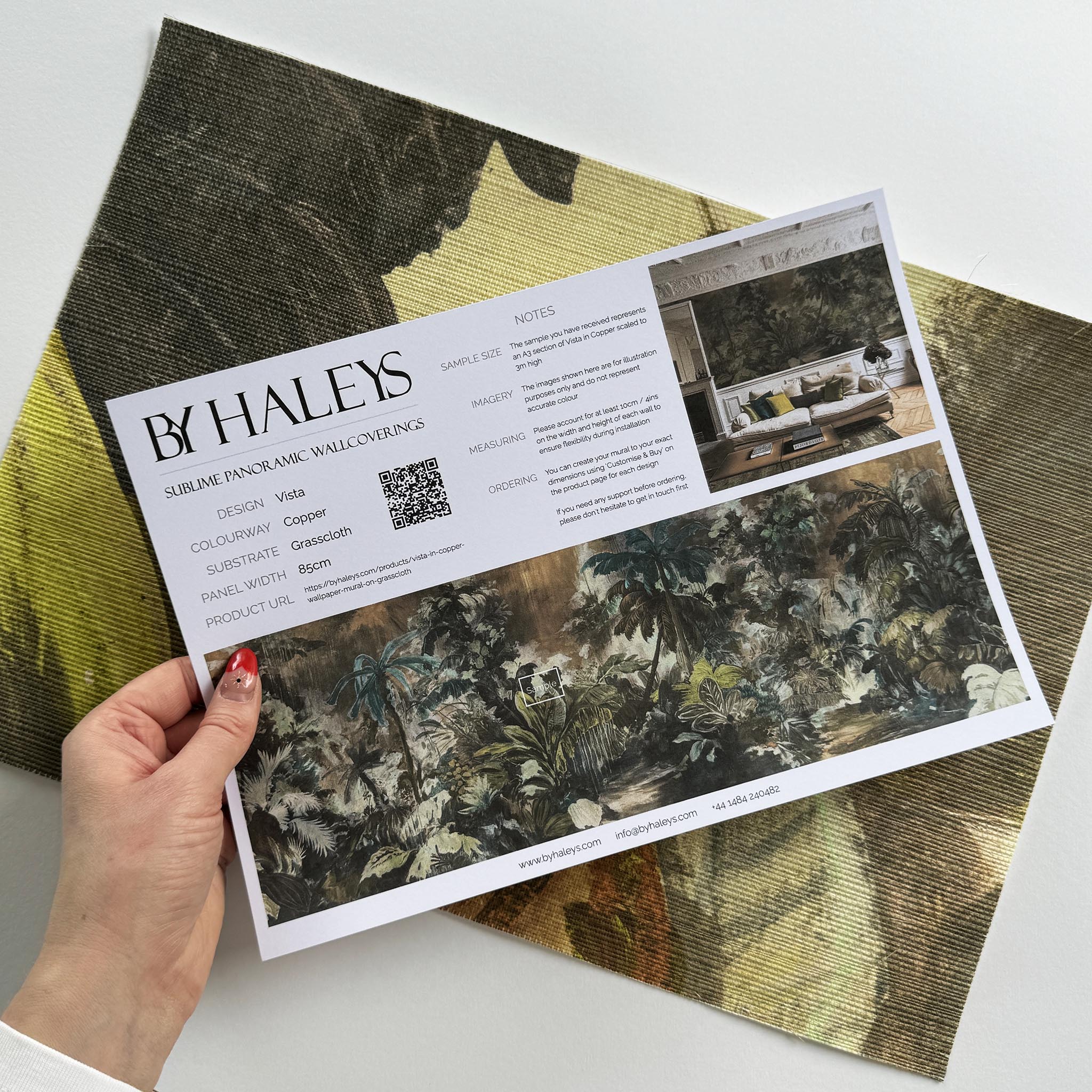 A hand showing information for a grasscloth wallpaper mural sample which features a moody jungle in teal and ochre.