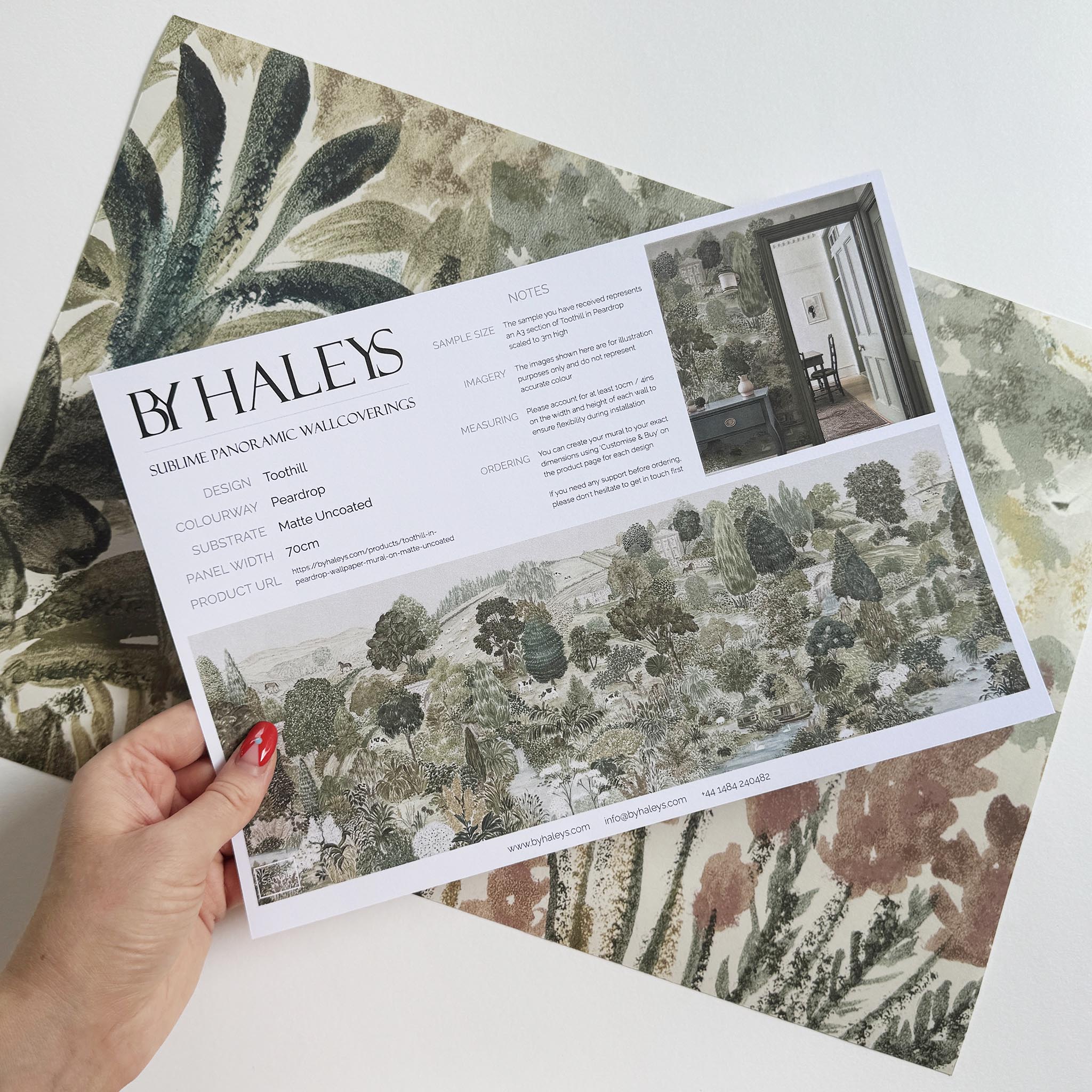 A hand showing information for a matte wallpaper mural sample which features a soft green countryside with cattle and boats