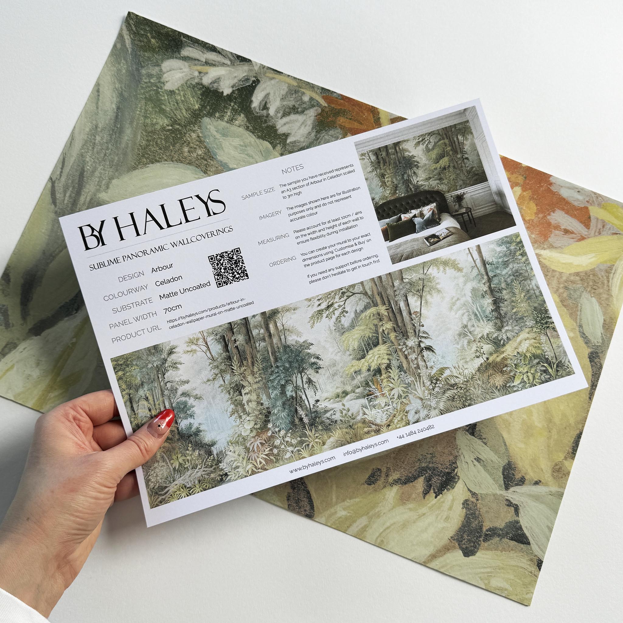 A hand showing information for a matte wallpaper mural sample which features an airy woodland in sage, yellow, and mist.