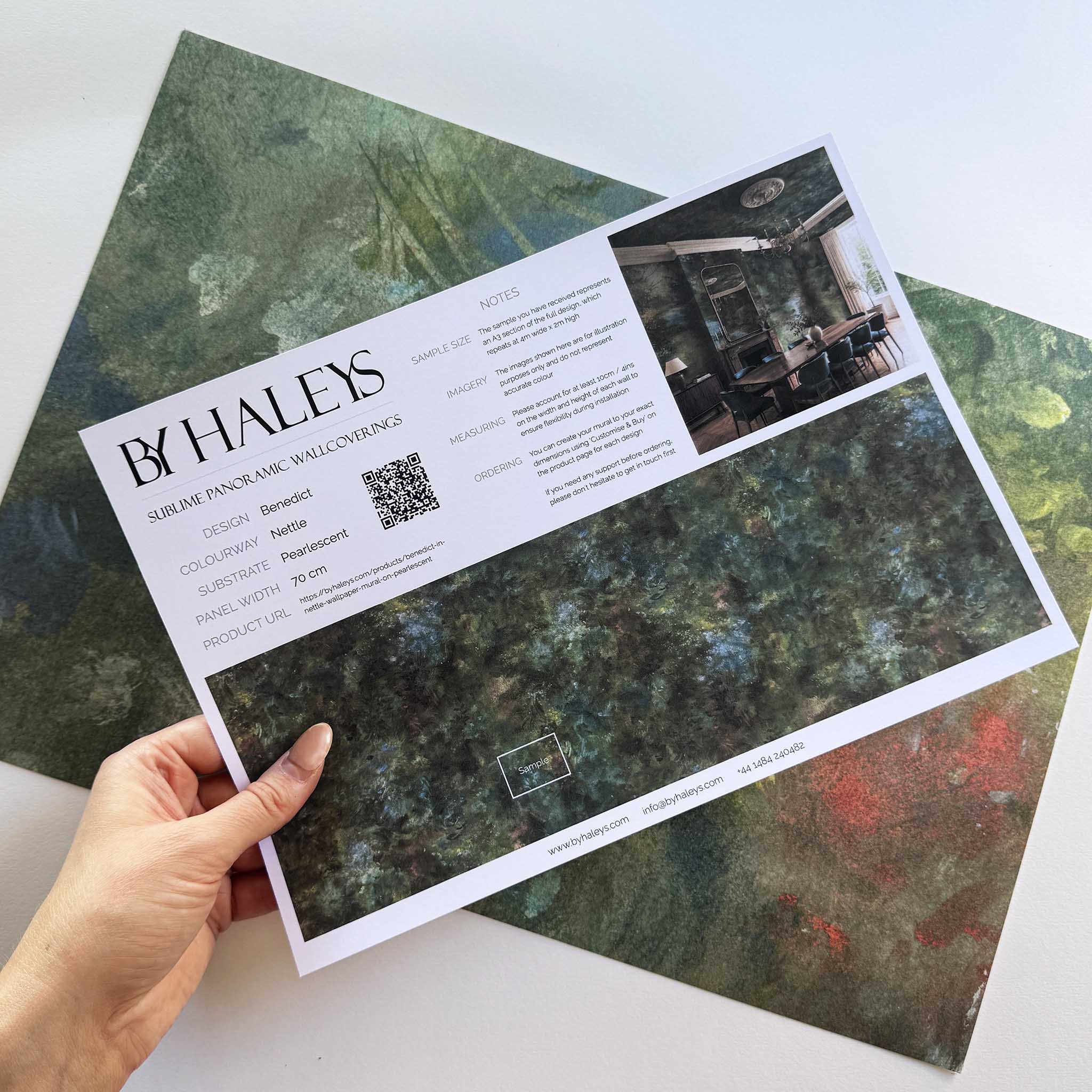 A hand showing information for a pearlescent wallpaper mural sample which features moody nettle-green mural with sage, charcoal and rust colours.