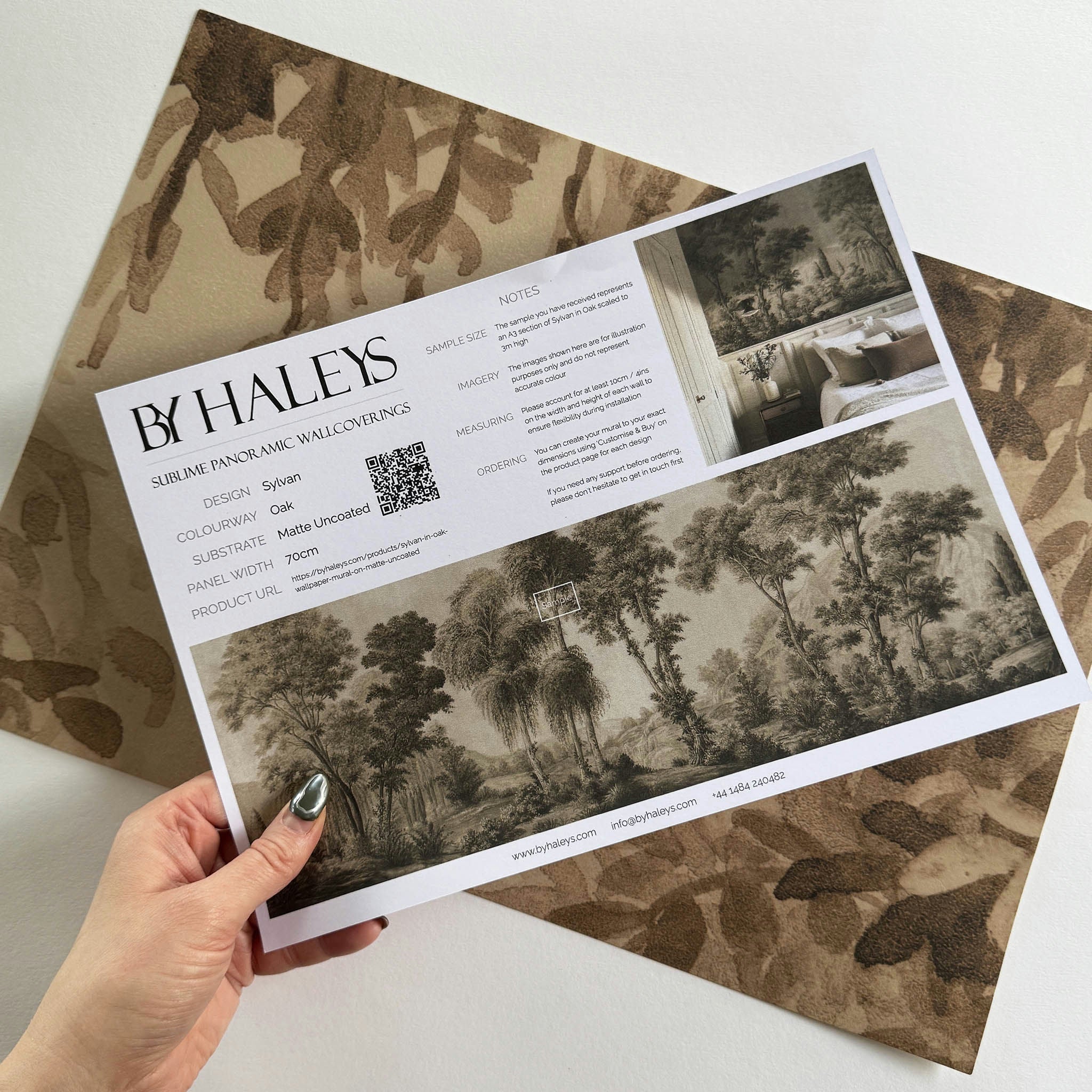 A hand showing information for a matte wallpaper mural sample which features sepia-toned woodland