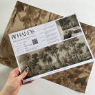 A hand showing information for a matte wallpaper mural sample which features sepia-toned woodland
