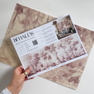 A hand showing information for a grasscloth wallpaper mural sample which features rose forest
