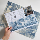 A hand showing information for a grasscloth wallpaper mural sample which features soft blue woodland