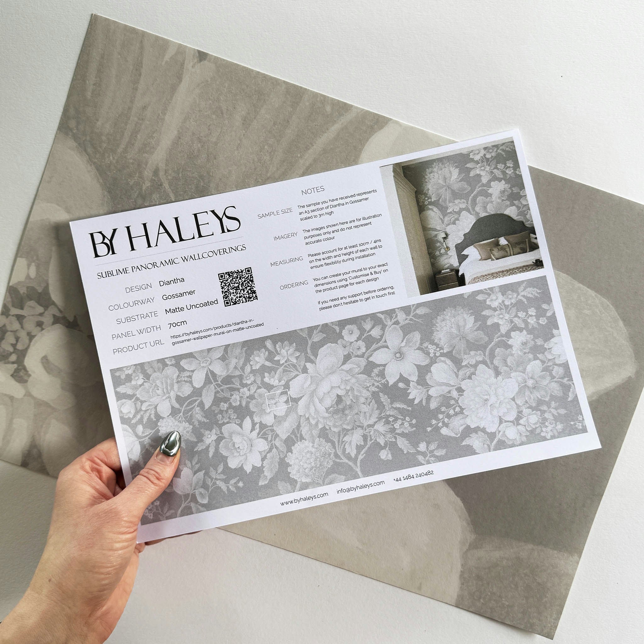 A hand showing information for a matte wallpaper mural sample which features misty whites on dove grey floral