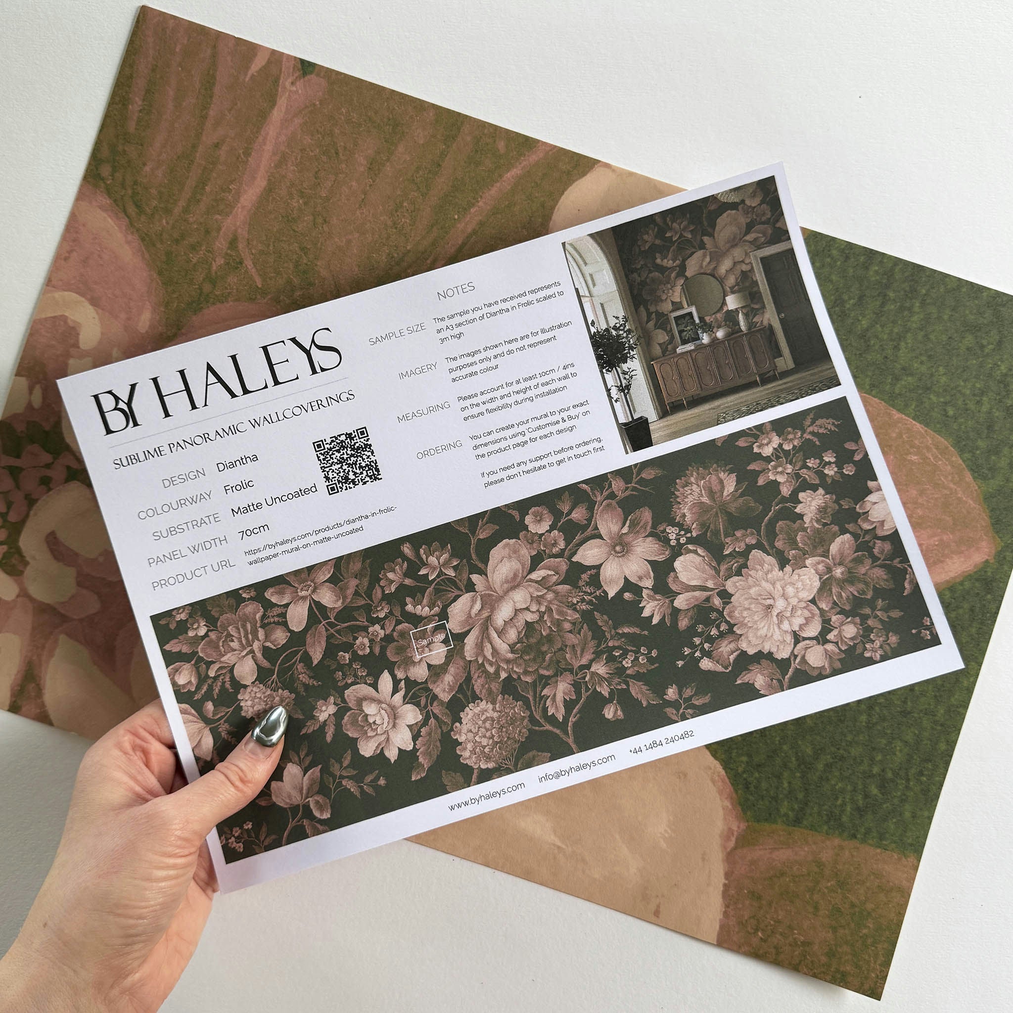 A hand showing information for a matte wallpaper mural sample which features rosy florals on lush green