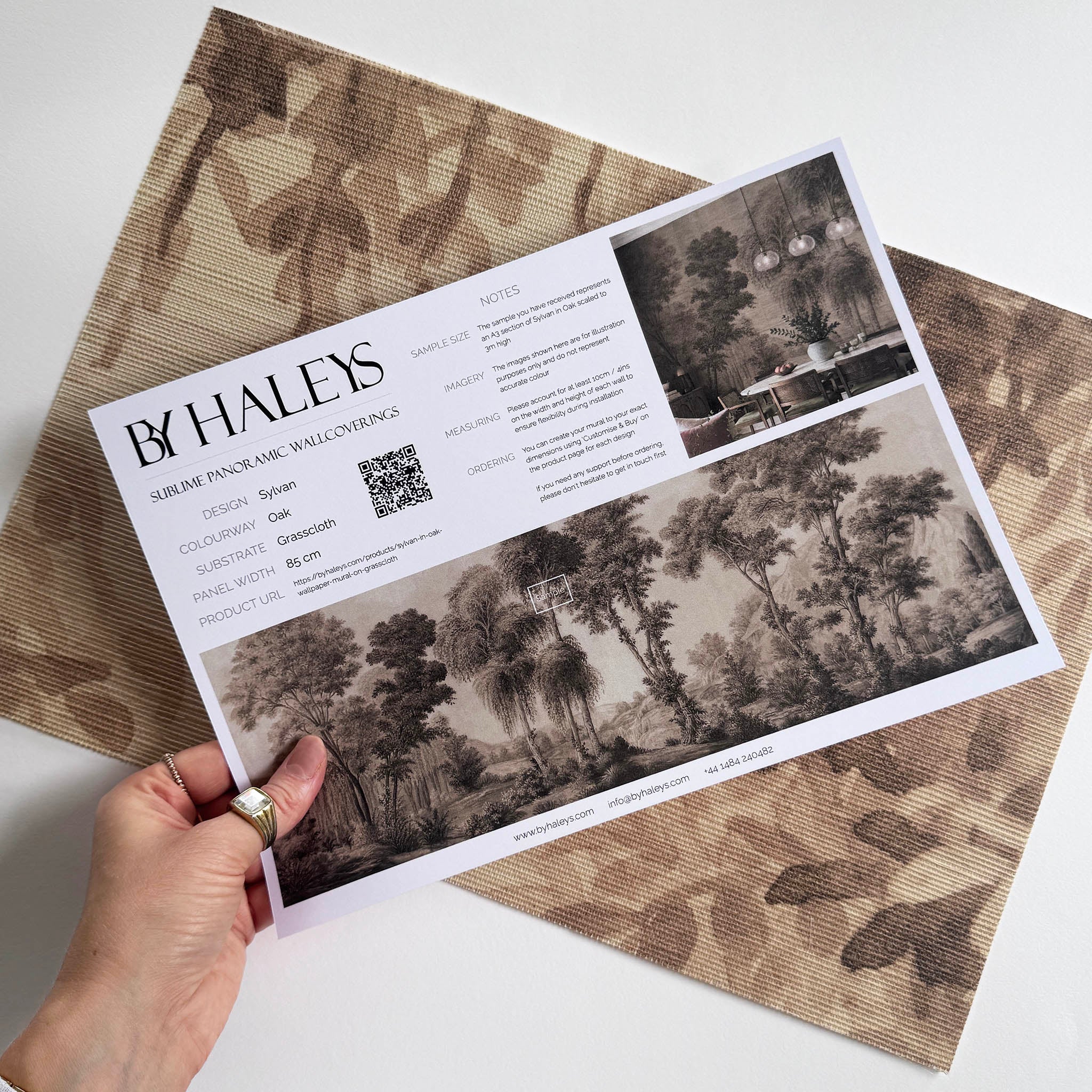 A hand showing information for a grasscloth wallpaper mural sample which features sepia-toned woodland
