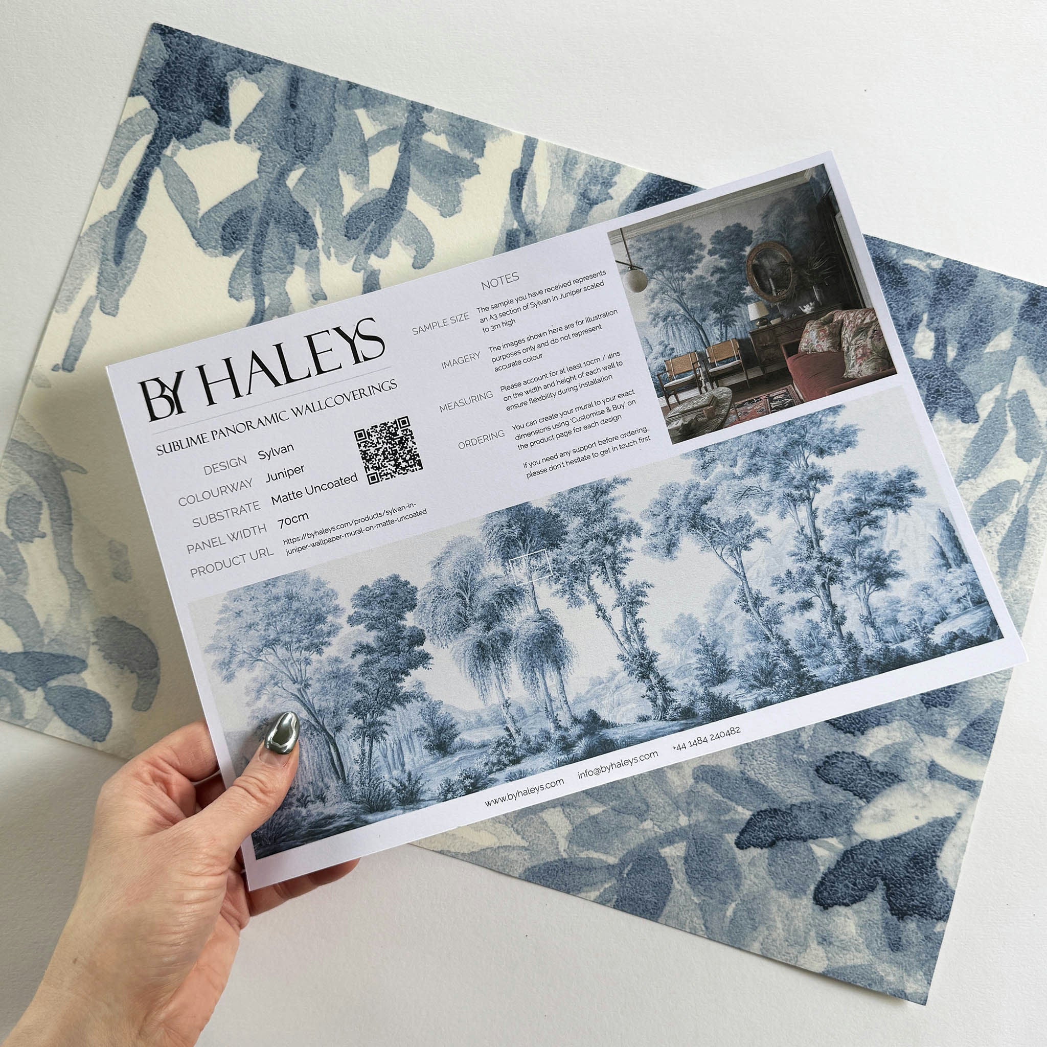 A hand showing information for a matte wallpaper mural sample which features soft blue woodland