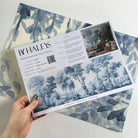 A hand showing information for a matte wallpaper mural sample which features soft blue woodland