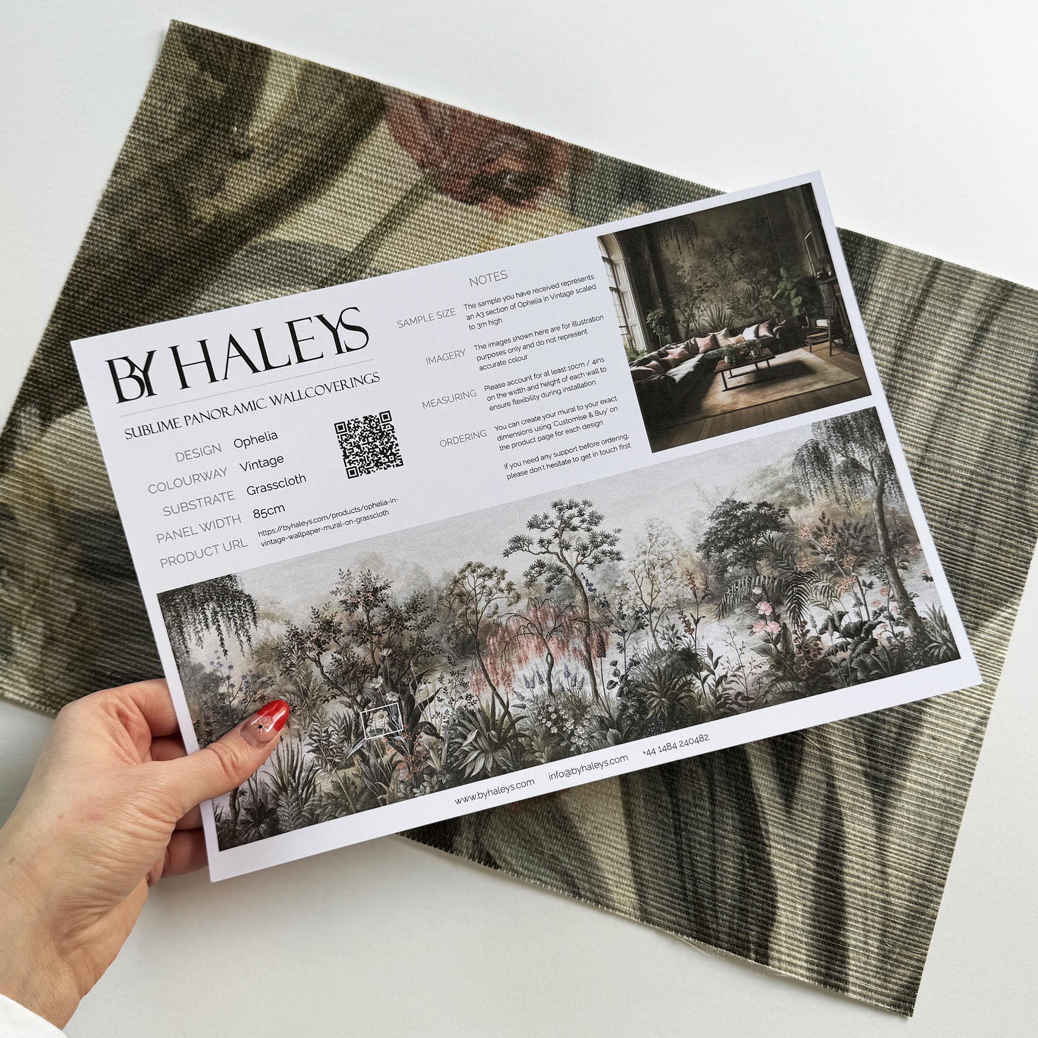 A hand showing information for a grasscloth wallpaper mural sample which features a lakeside scene in vintage tones.