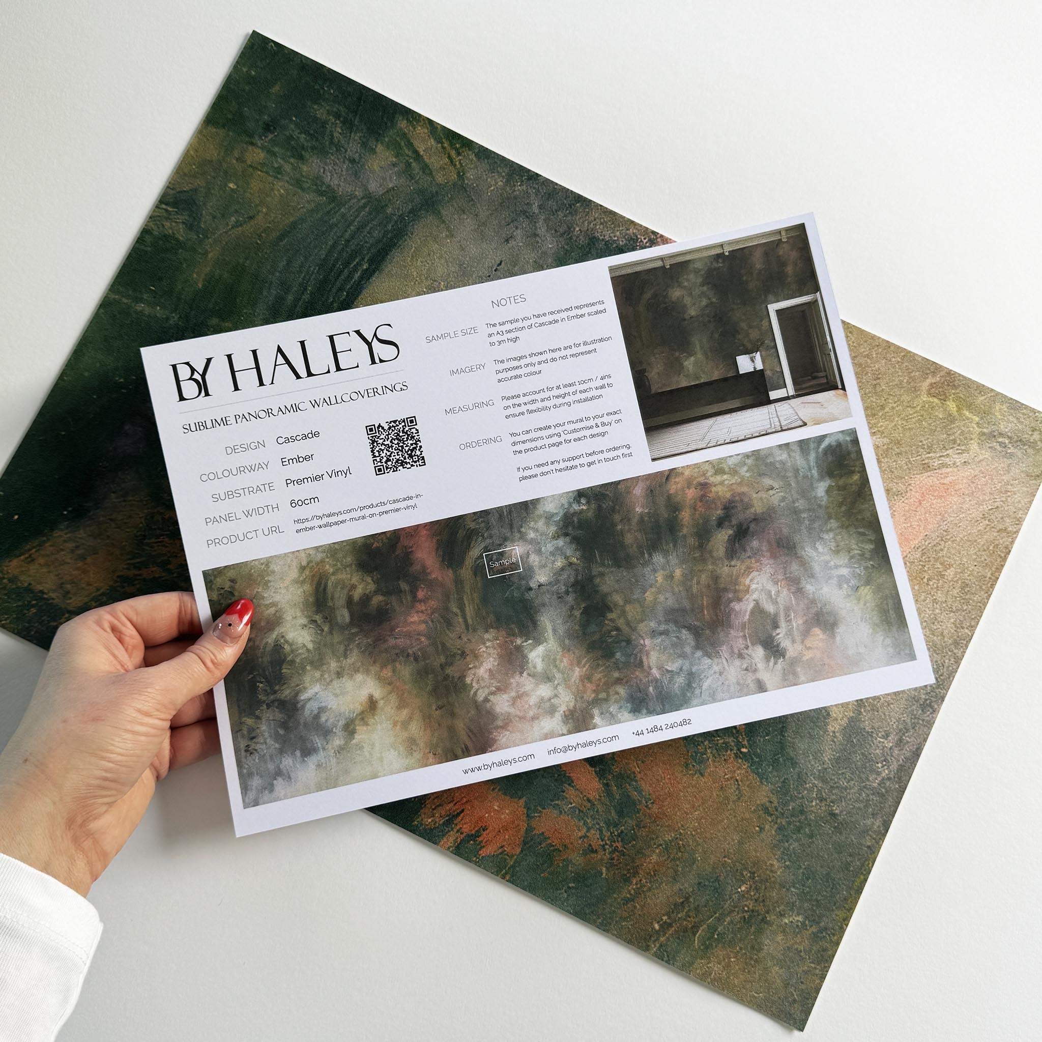 A hand showing information for a vinyl wallpaper mural sample which features an abstract haze in green and blush.