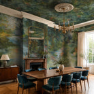 An interior dining room featuring a panoramic pearlescent wallpaper mural of moody nettle-green mural with sage, charcoal and rust colours.